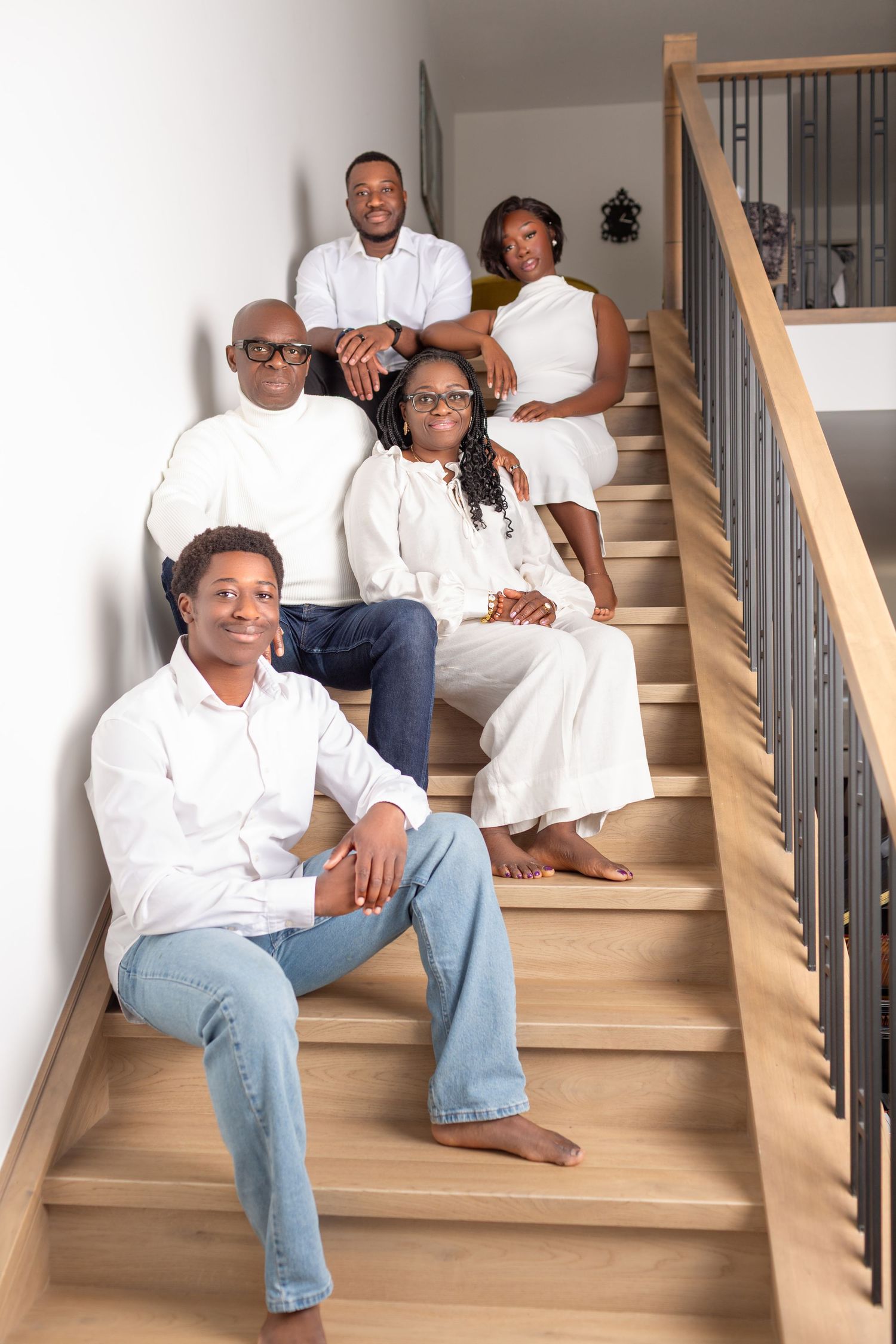 Family of five in white outfits posing on modern wooden staircase.