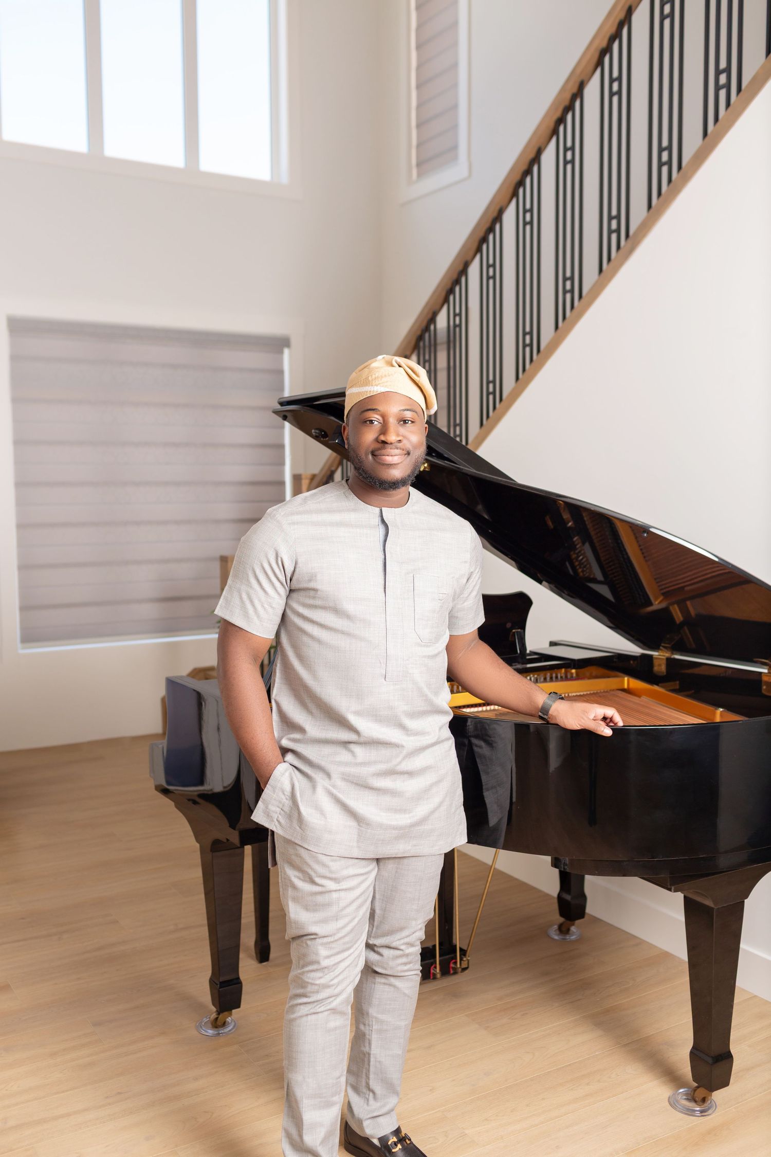 Smiling man in traditional African attire stands beside a grand piano in an elegant home interior.