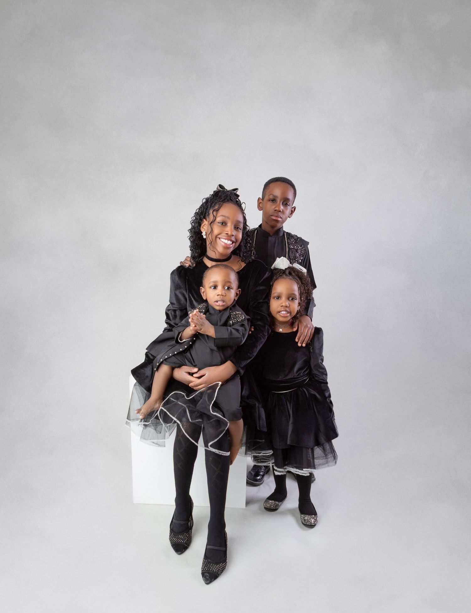 Family portrait of a mother and three children dressed in matching black outfits posing together in a studio.