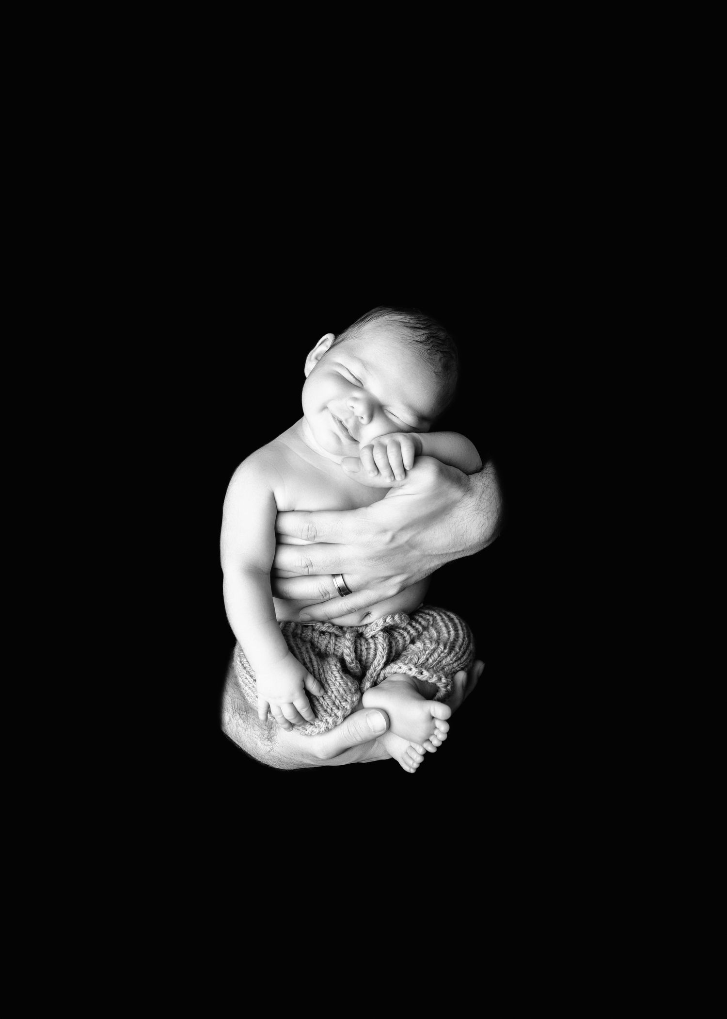 Black and white photo of a sleeping newborn baby cradled gently in adult hands against dark background.