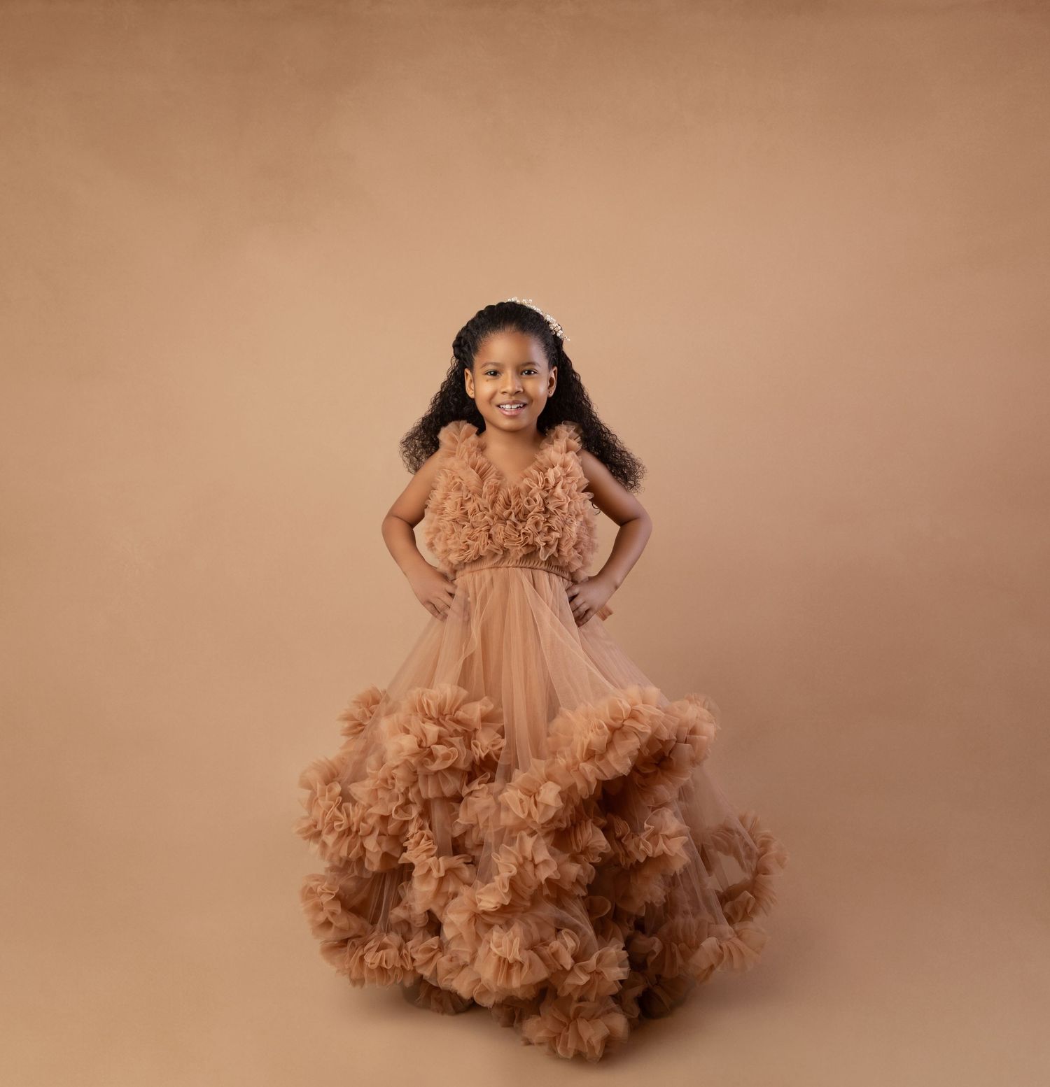 Young girl in a stunning ruffled tan tulle ball gown posing confidently in a professional photo studio.