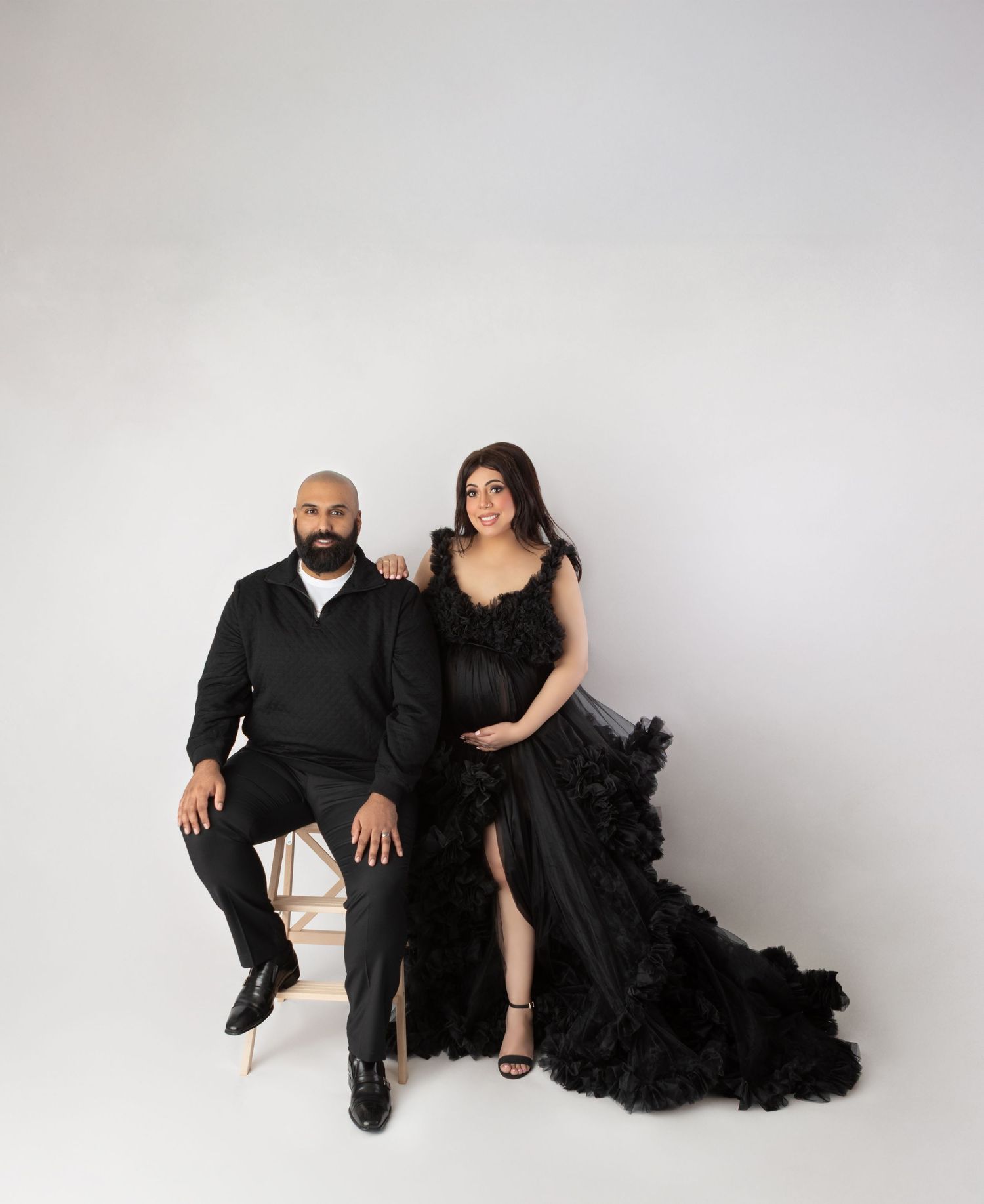 Couple maternity photo with woman in black ruffled gown and man in black attire.