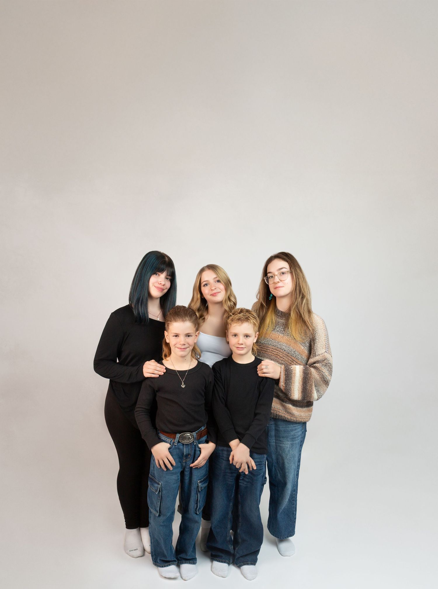 Group of five siblings, three girls and two boys, pose together against a light gray background.