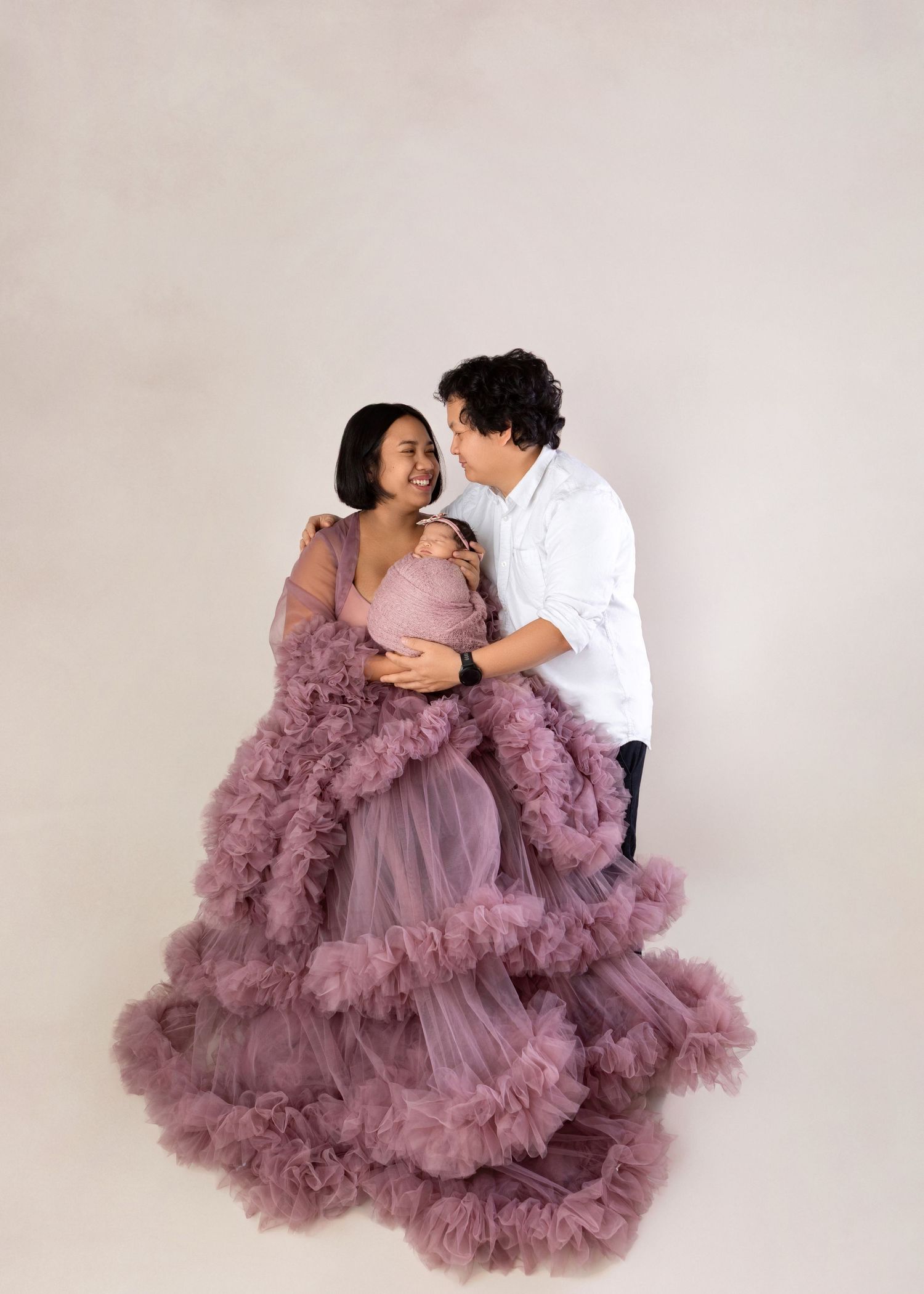 Couple in maternity photo shoot, woman in elegant purple ruffle gown embraced by man in white shirt.