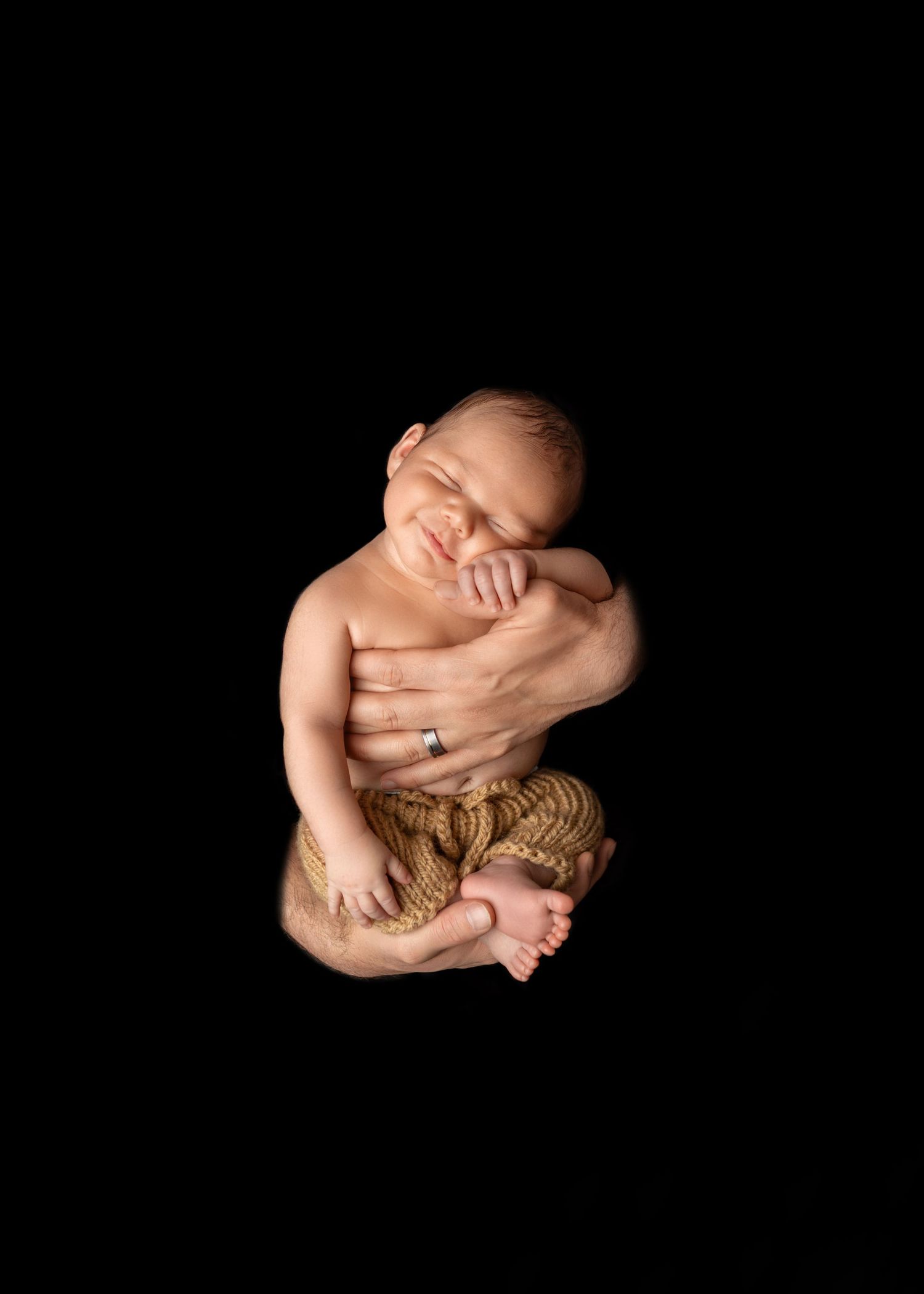Newborn baby sleeping peacefully, cradled in parent's hands against black background, wrapped in golden rope.