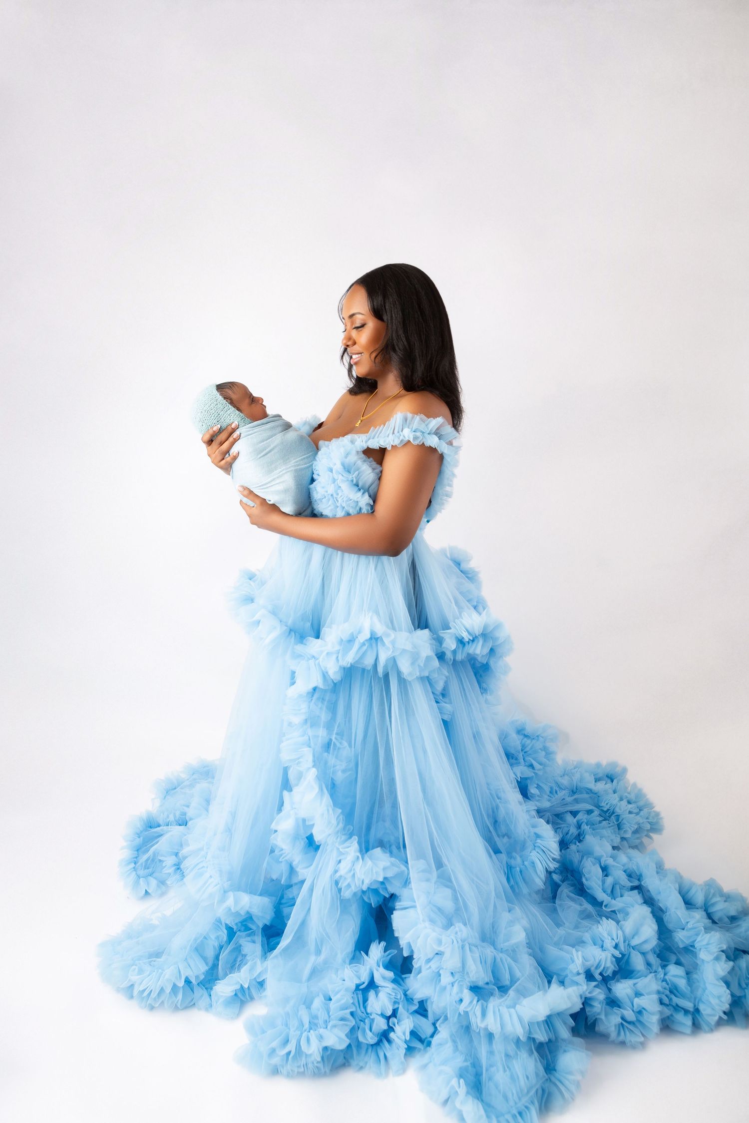 Woman in blue ruffled tulle gown holding newborn baby in studio portrait.