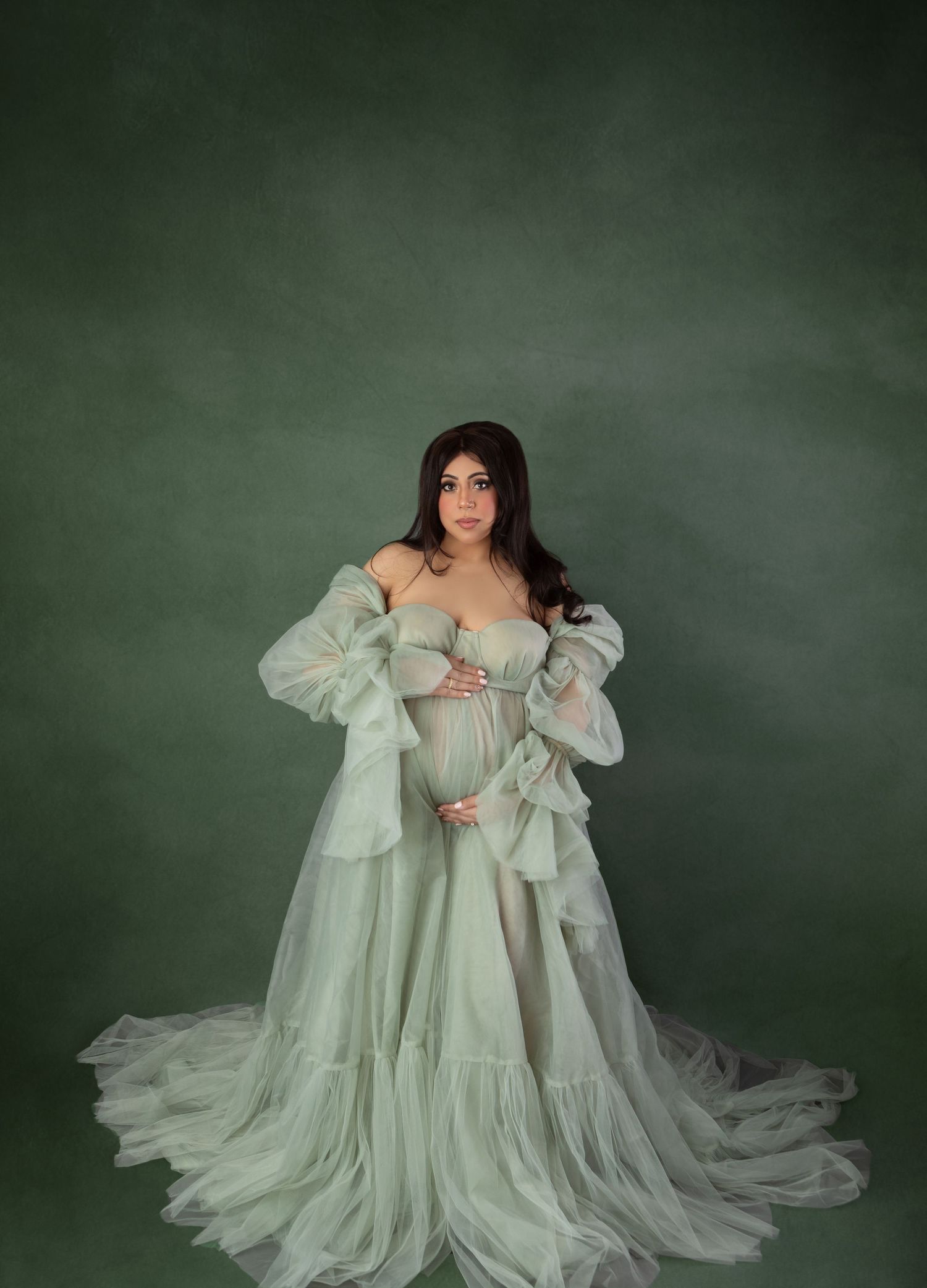 Pregnant woman in sage green ruffled off-shoulder maternity gown in studio portrait.