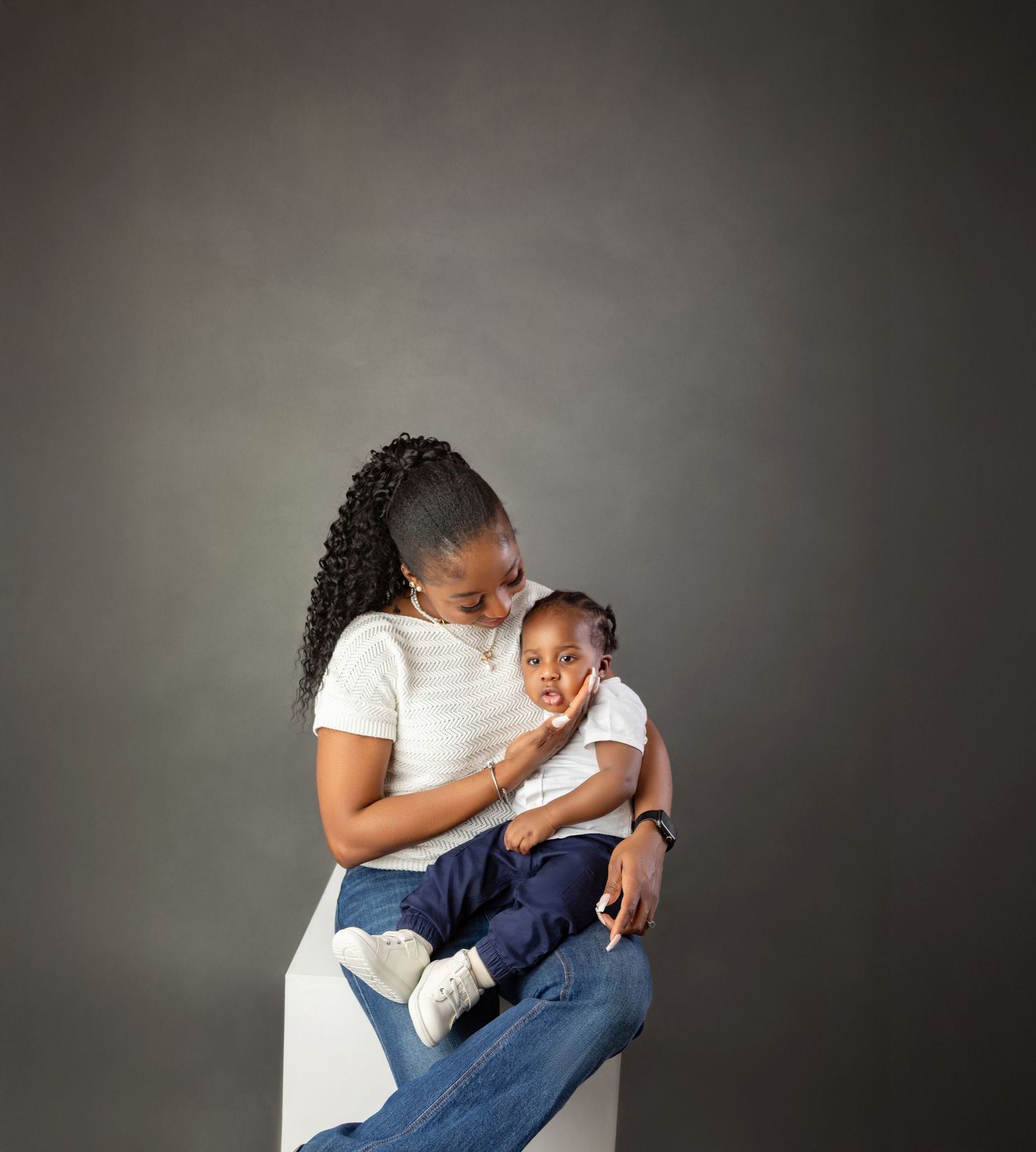 Young woman in white top holding baby in studio portrait on gray background.