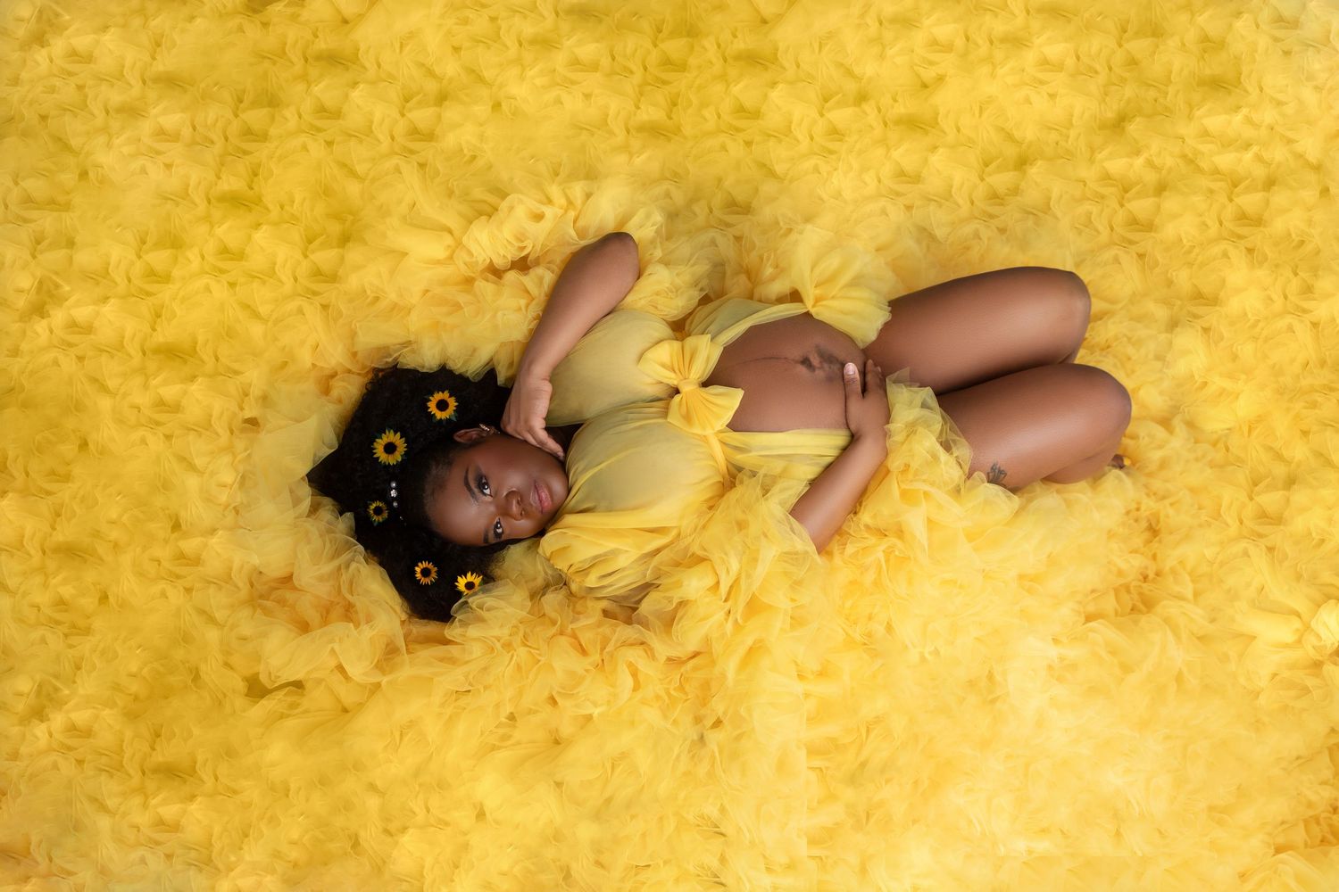 Young girl in yellow outfit lying on a fluffy yellow feather background in a studio photo shoot.