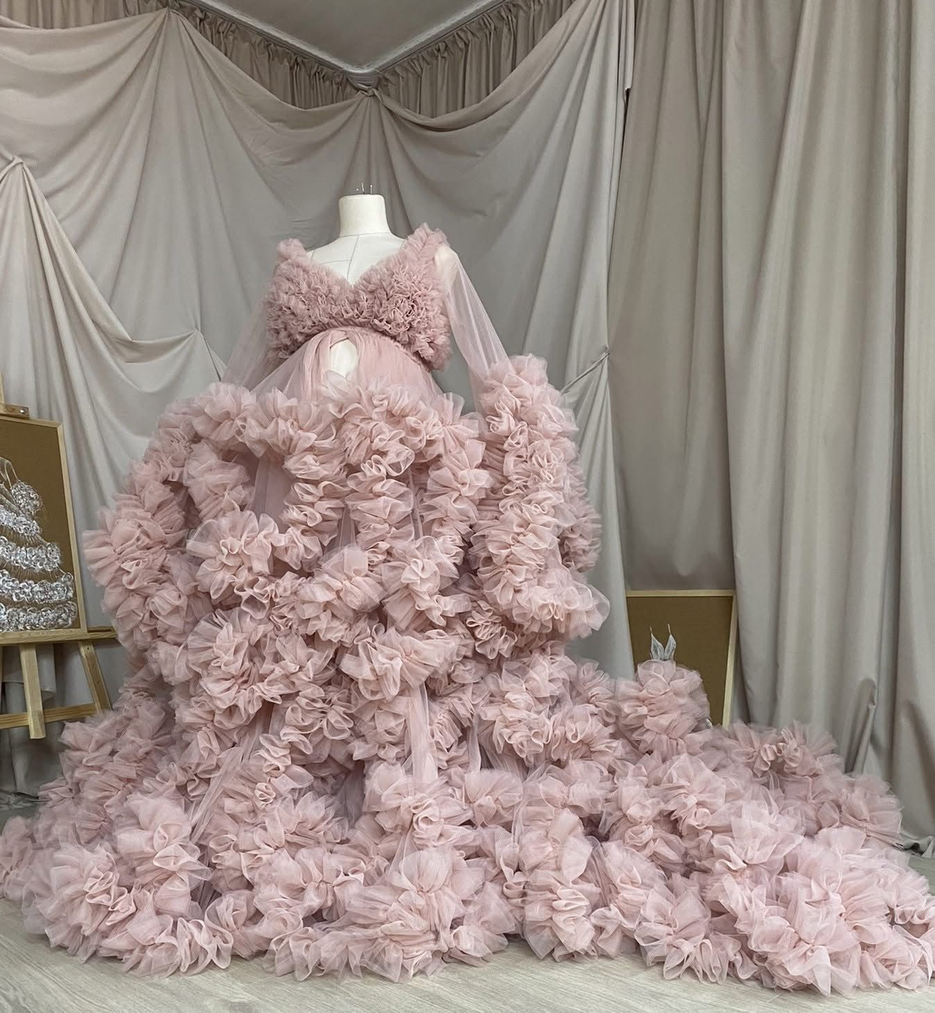 Blush pink ruffled tulle maternity gown with long sleeves and dramatic floral train for photoshoots.
