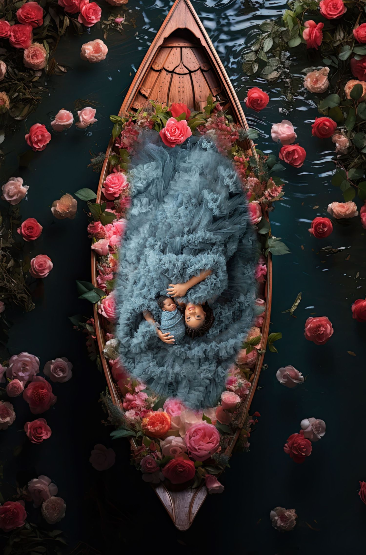 Child lying in a flower-adorned wooden boat surrounded by pink roses on dark water, draped in blue fabric.