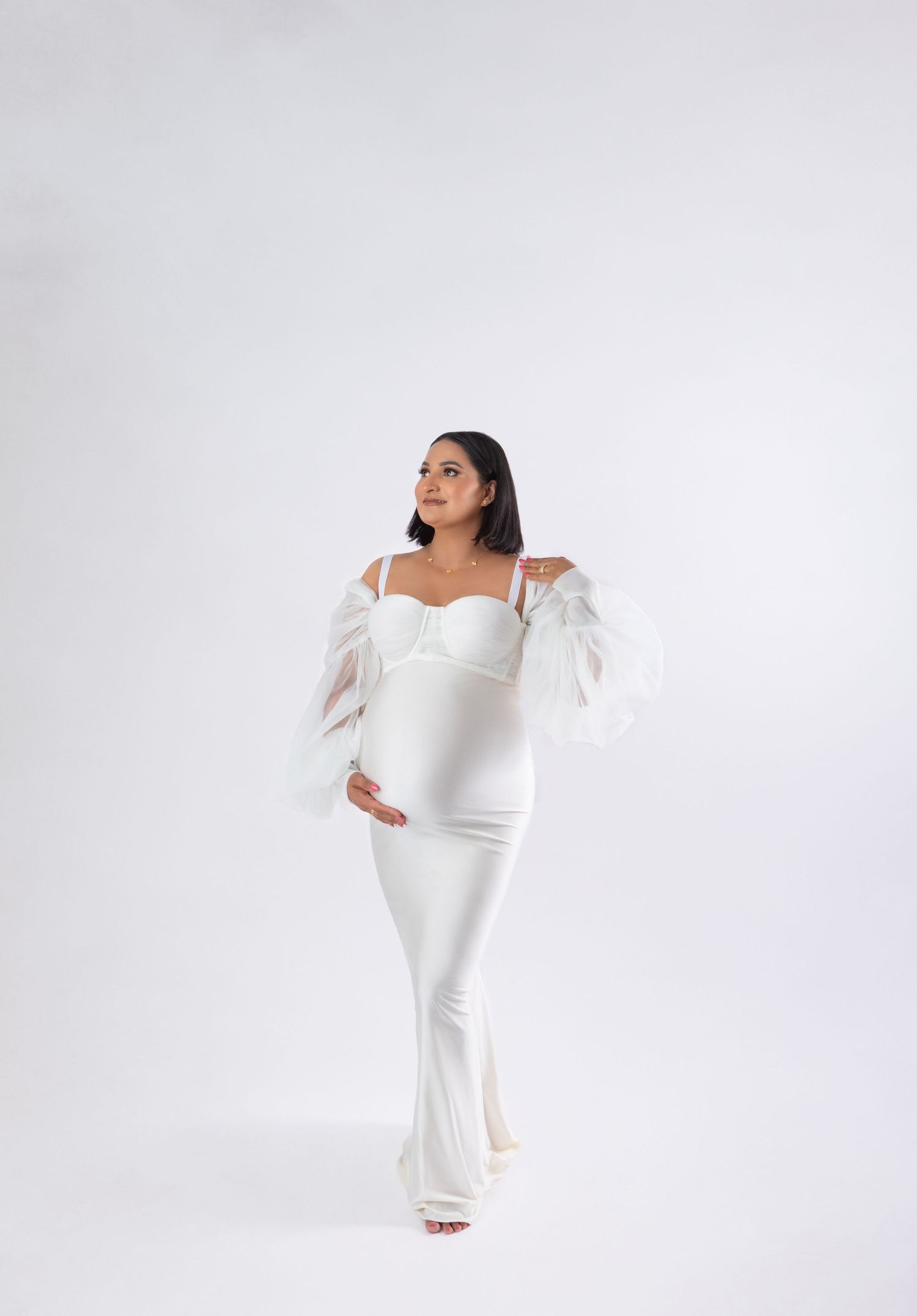 Woman in white off-shoulder mermaid gown with sheer puff sleeves and bustier bodice, posing elegantly.