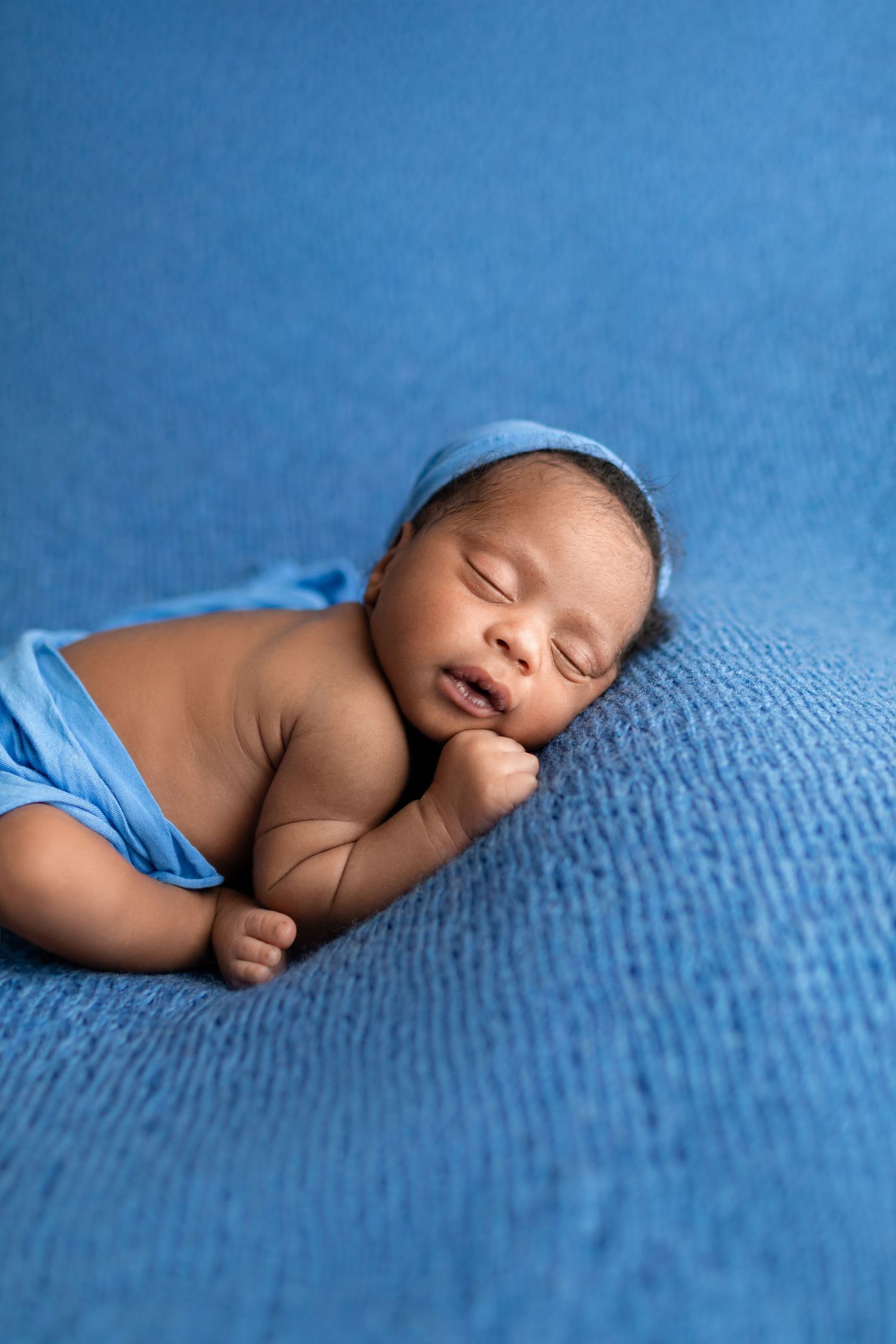 Sleeping newborn in blue wrap and bonnet on blue textured blanket.