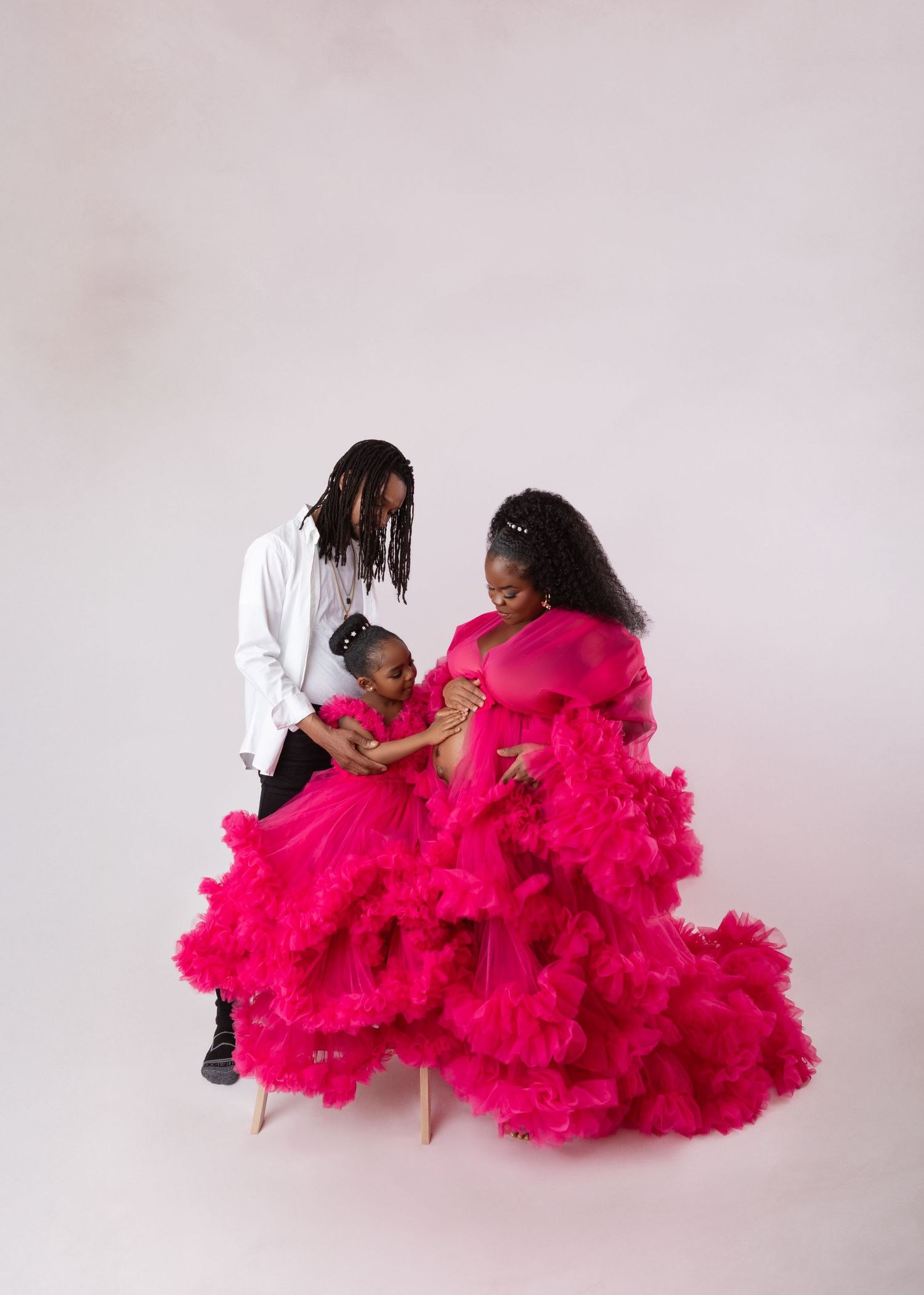 Family maternity photo with parents and daughter in matching hot pink voluminous tulle gowns.