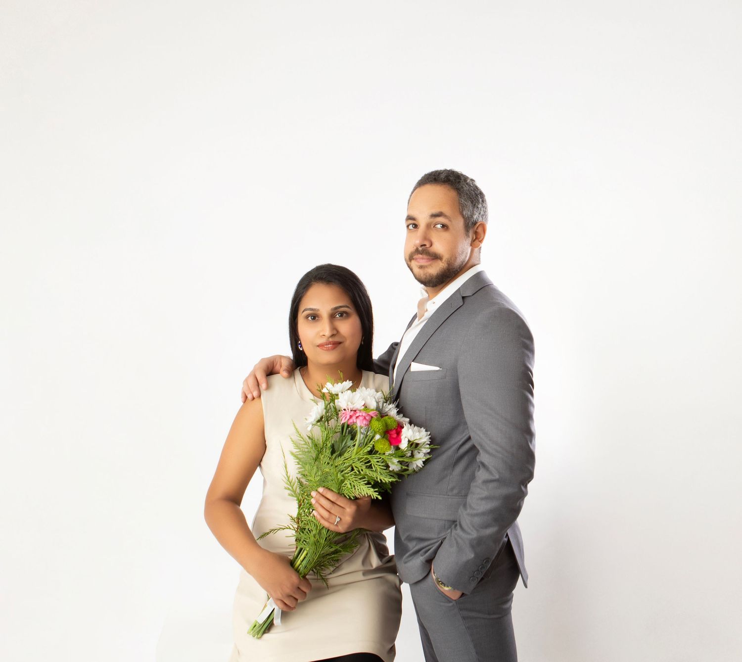Elegant couple posing with colorful flower bouquet against white studio background.