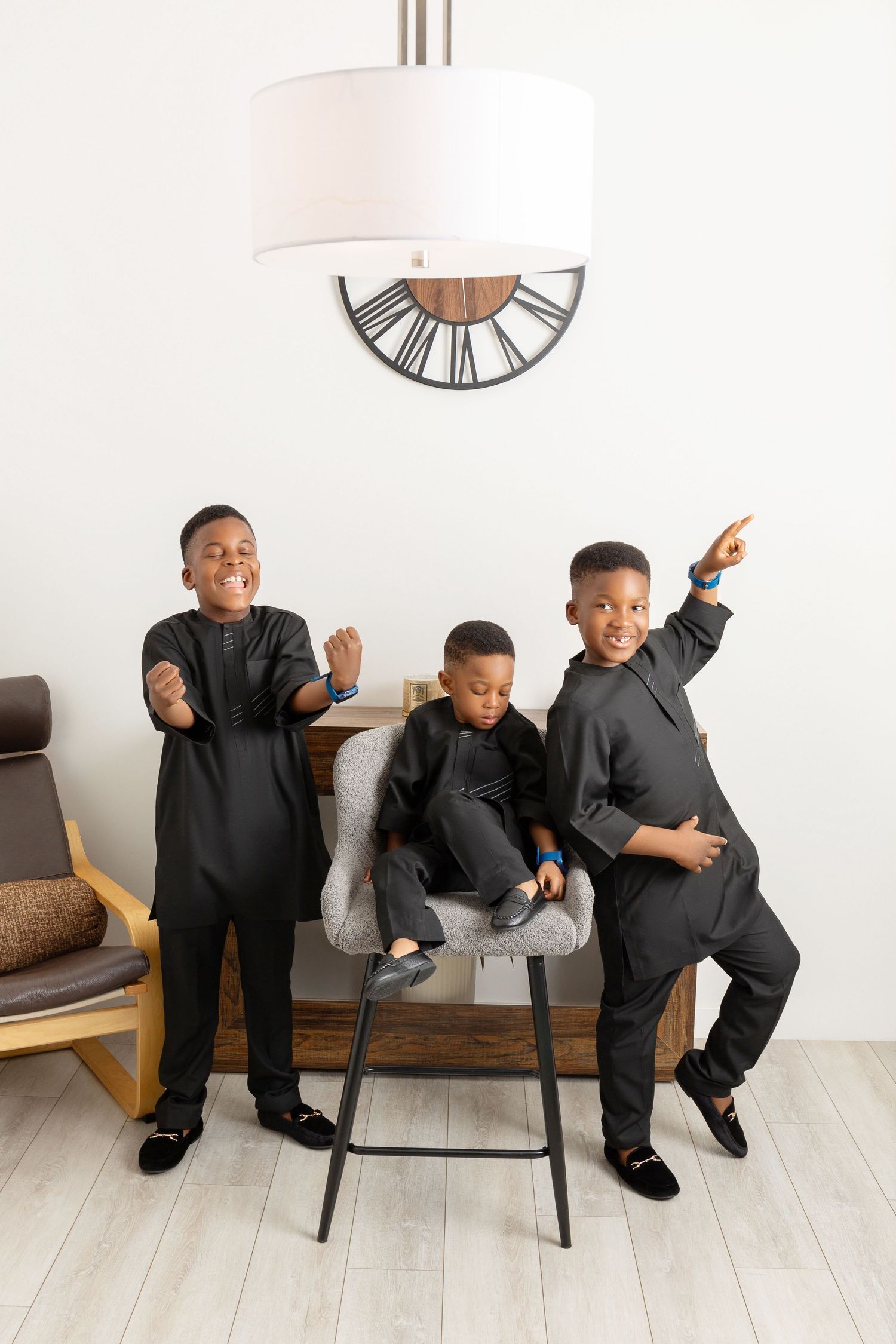 Three young boys in matching black traditional outfits pose energetically in a bright modern living room.