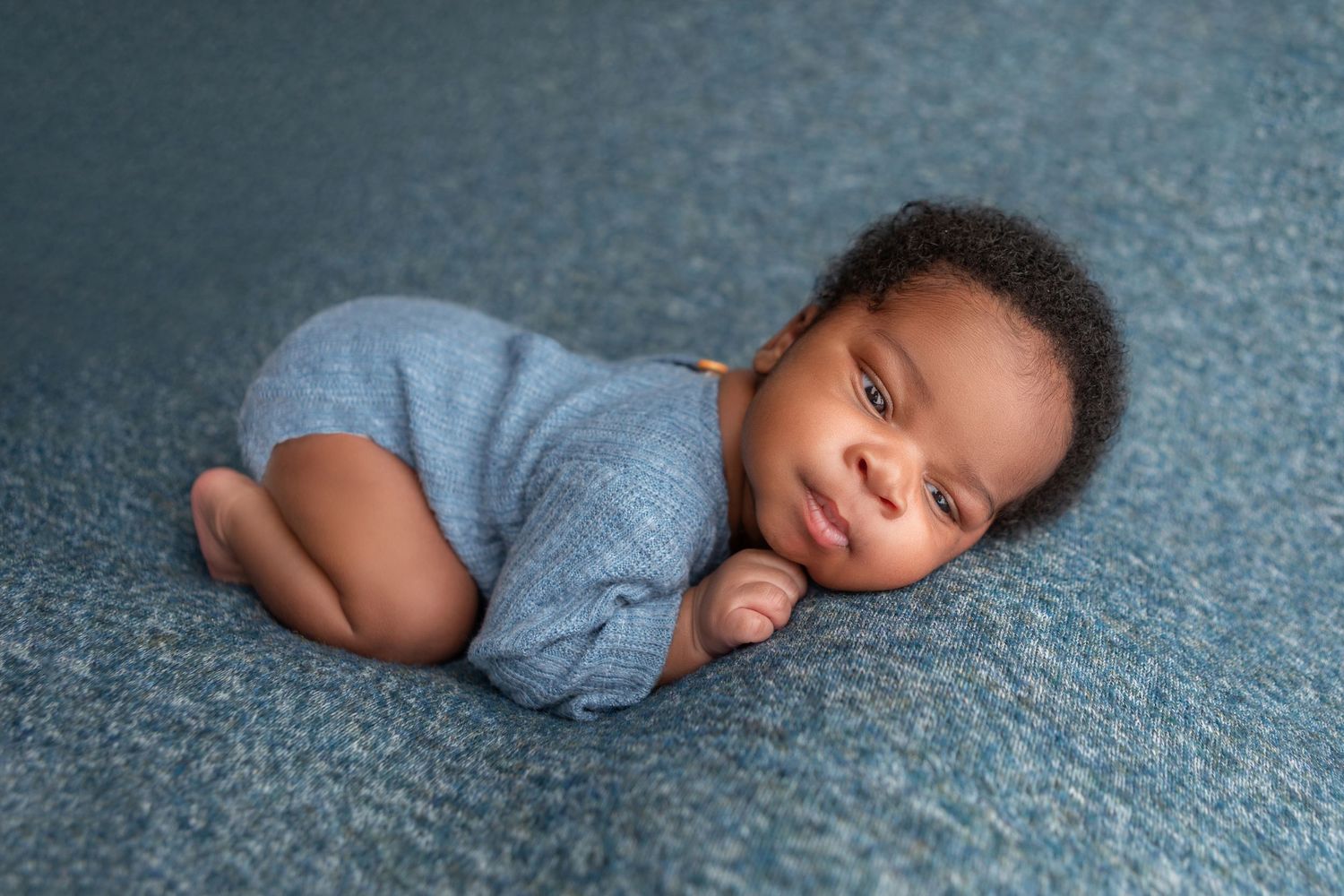 Adorable newborn baby smiling while lying on a teal blanket wrapped in a blue swaddle.