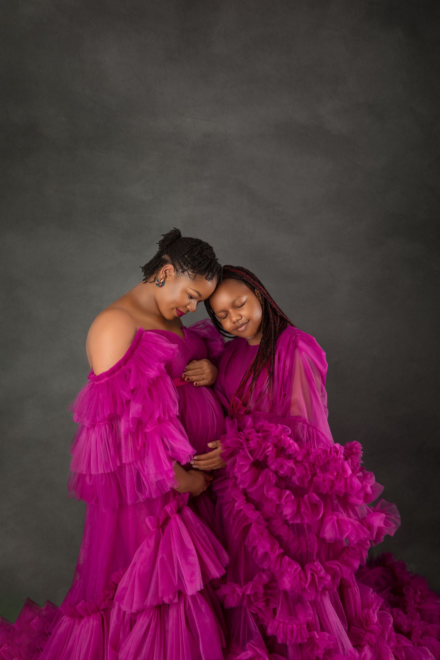 Two women in magenta ruffle tulle gowns share a tender moment during a maternity photoshoot.