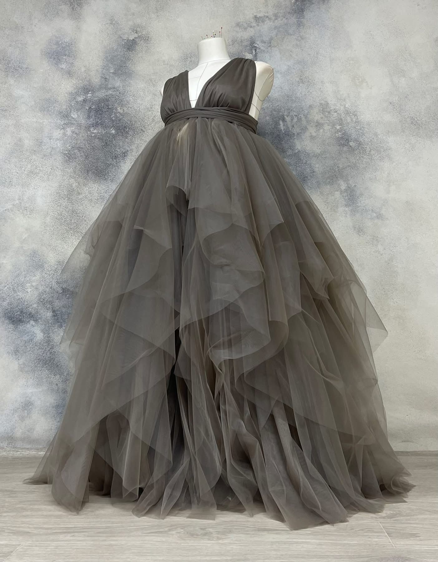 Charcoal gray layered tulle ballgown with V-neck and cascading asymmetrical skirt on dress form.