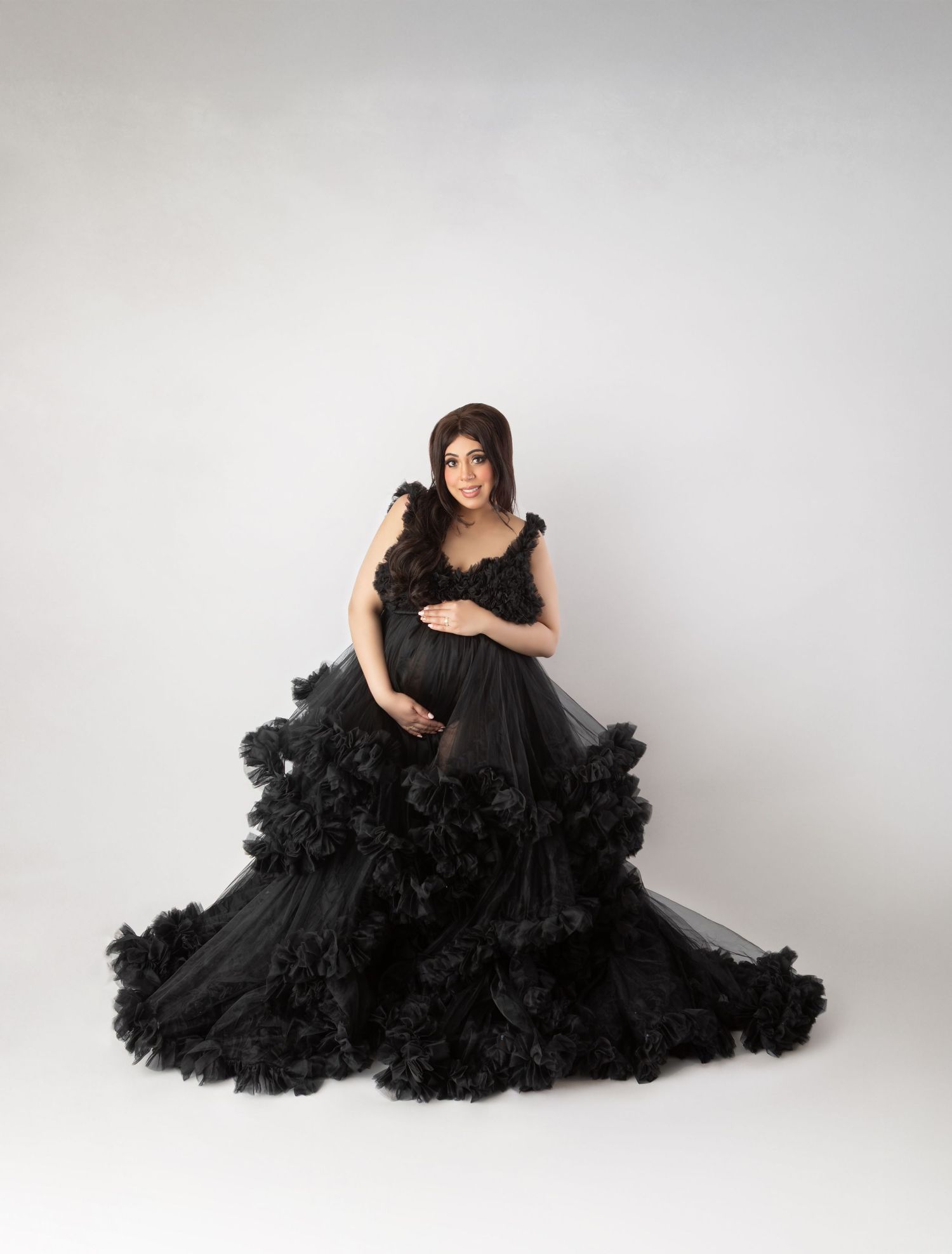Pregnant woman in stunning black ruffled tulle maternity ball gown studio portrait.
