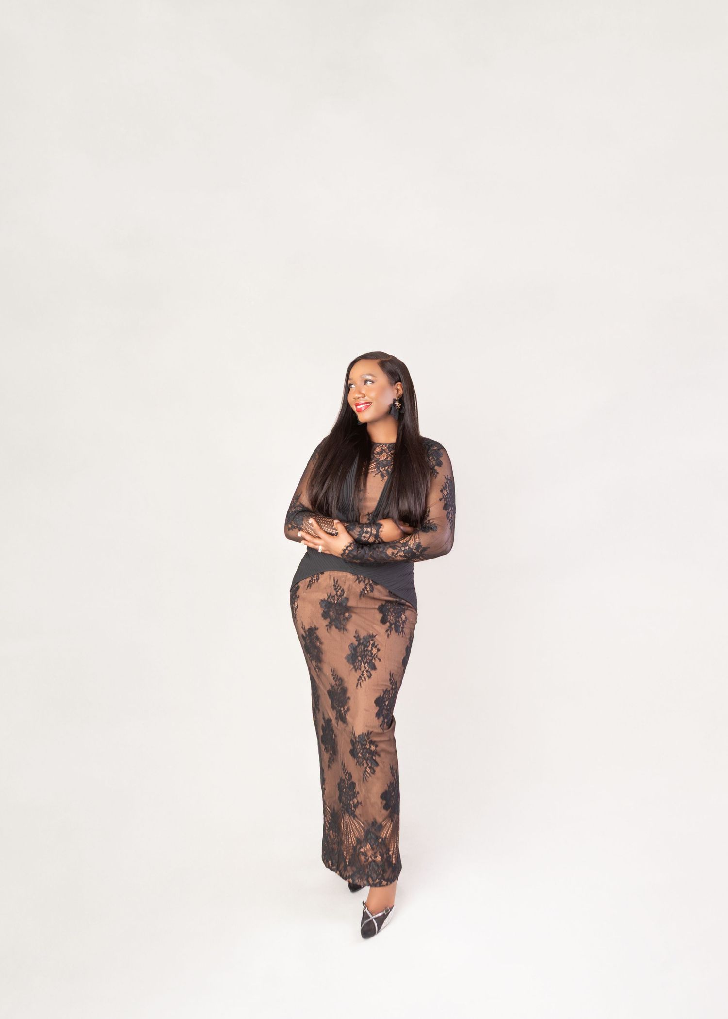 Woman in black floral lace sheer maxi dress with long sleeves, posing against white background.