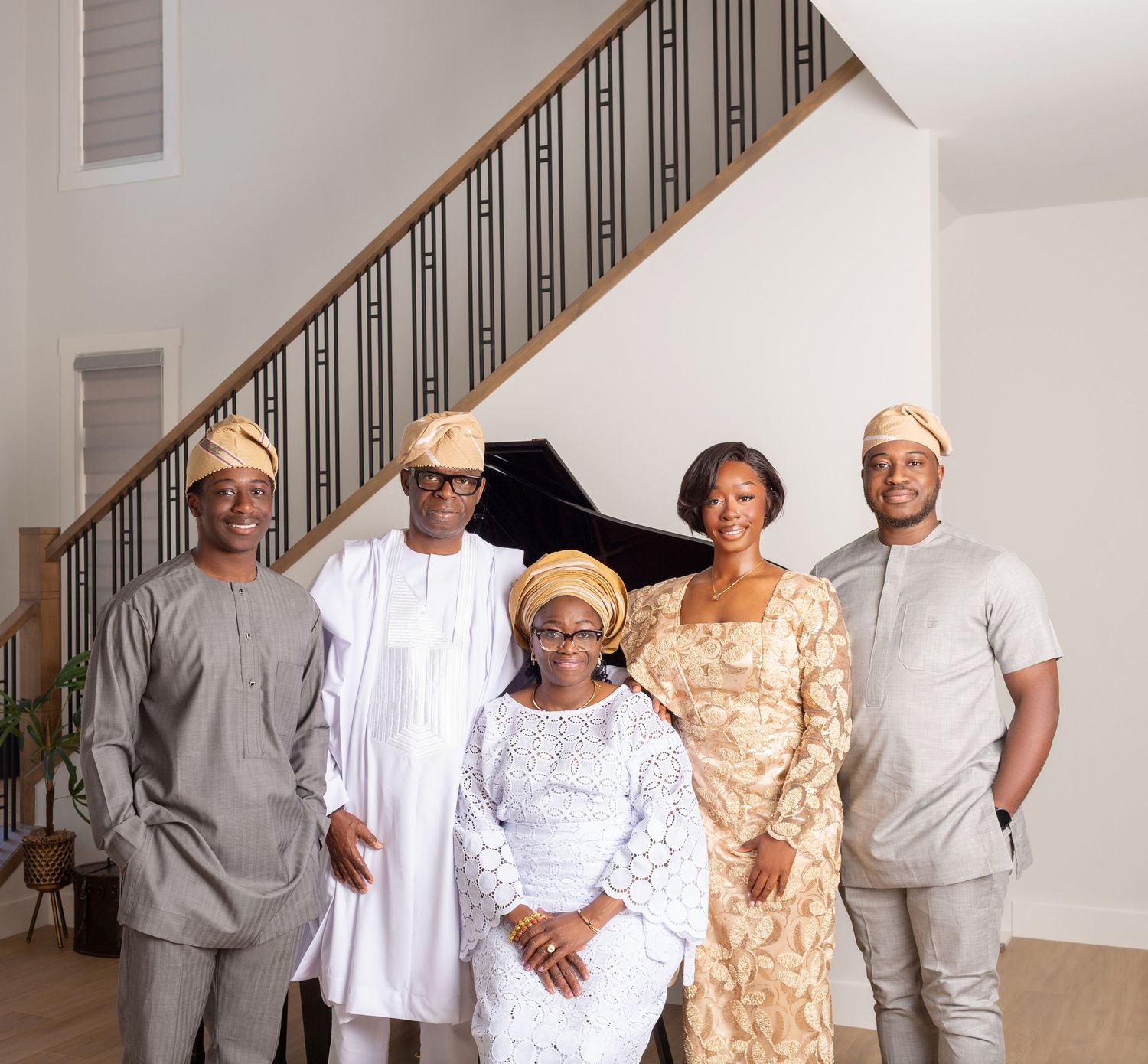 Five people in traditional Nigerian attire pose together near a staircase in an elegant home setting.