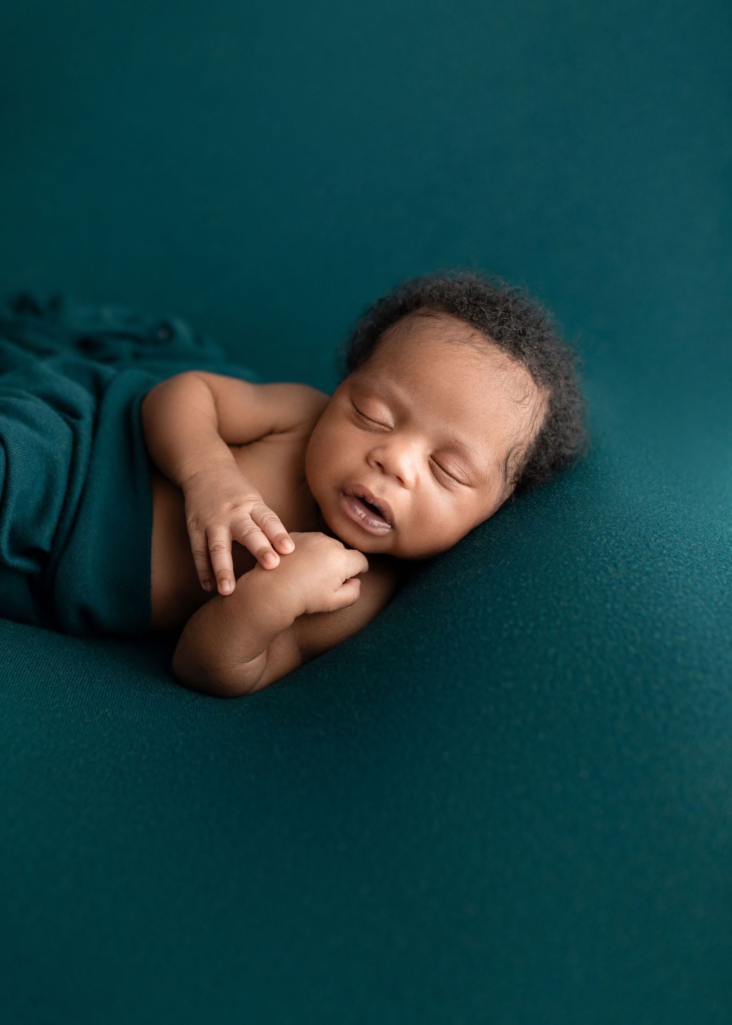 Newborn baby sleeping on teal blanket with teal fabric wrap.