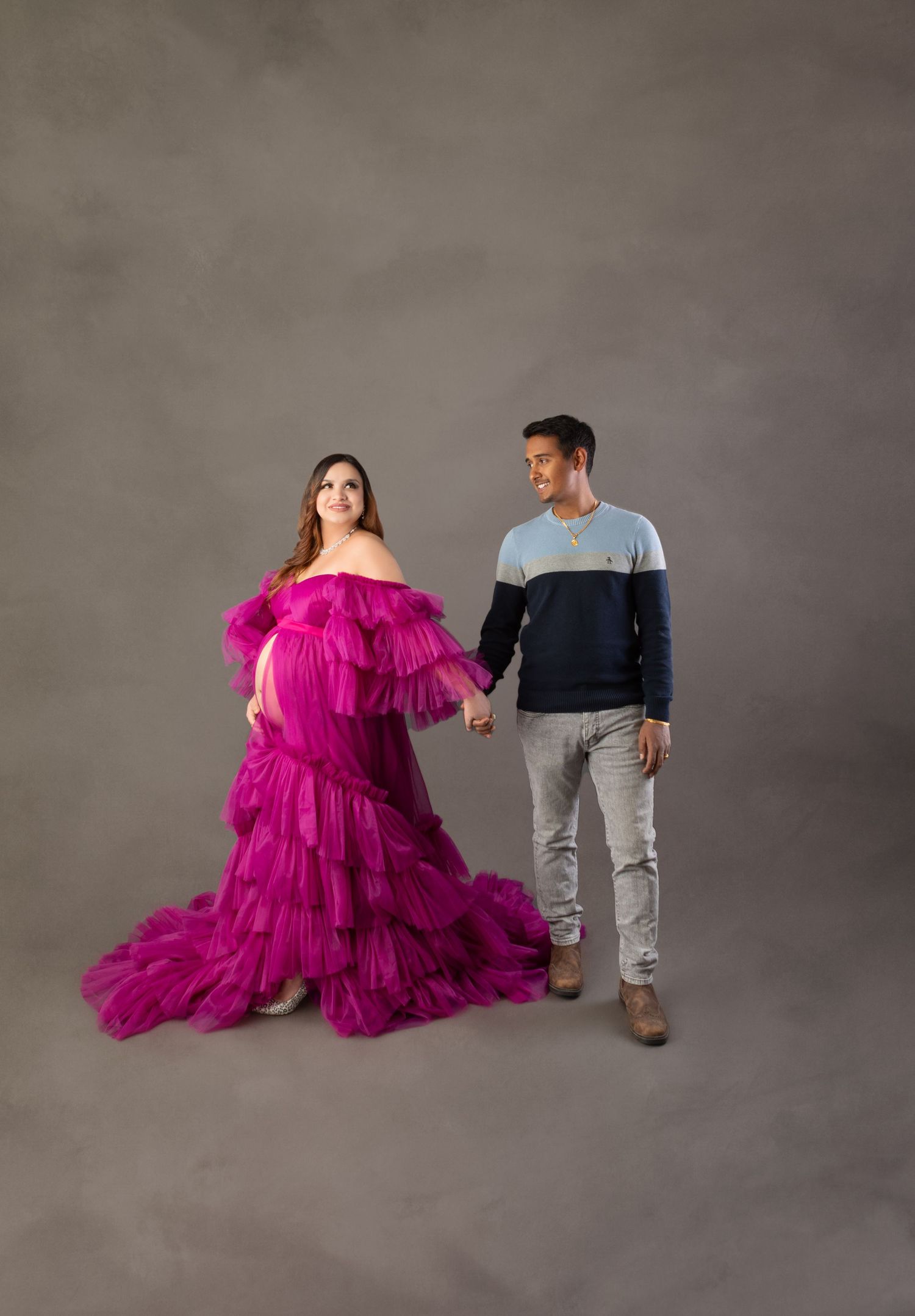 Pregnant woman in vibrant magenta ruffled tulle gown holding hands with partner during maternity shoot.