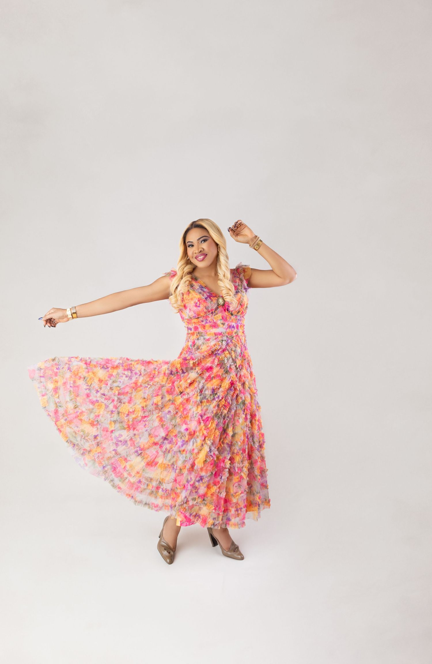 Woman twirling in a vibrant pink floral maxi dress with ruffles against a white background.