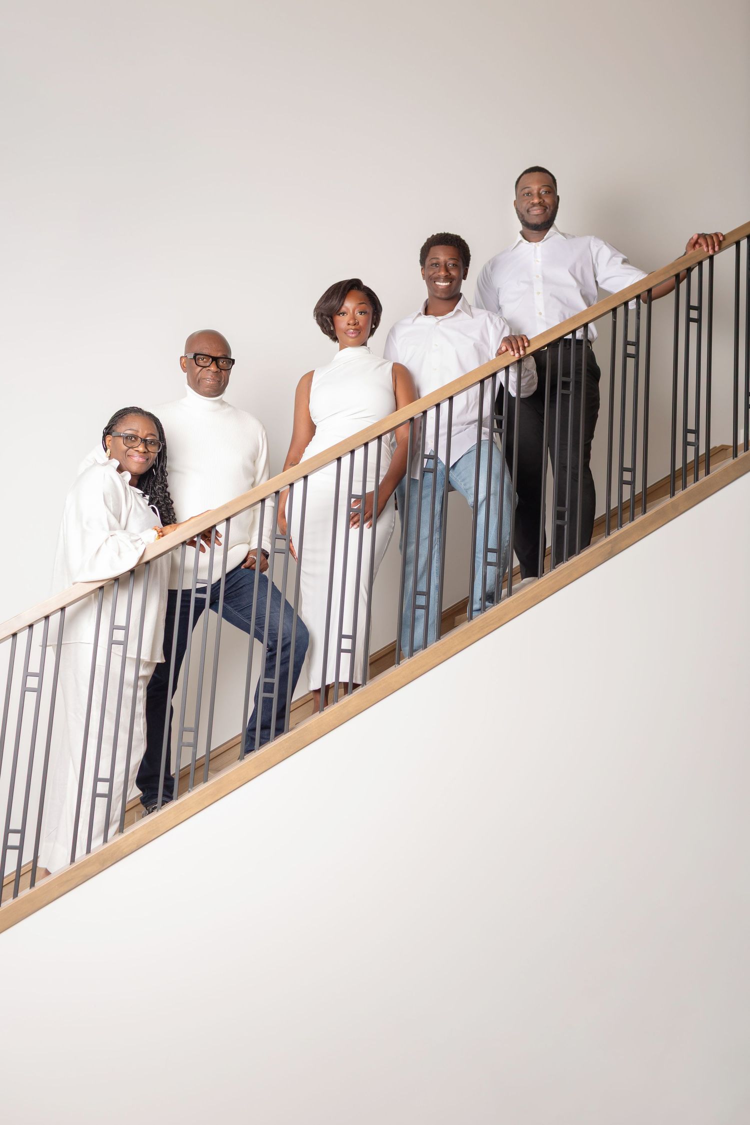 Five people dressed in white pose together on a modern staircase with metal railings.