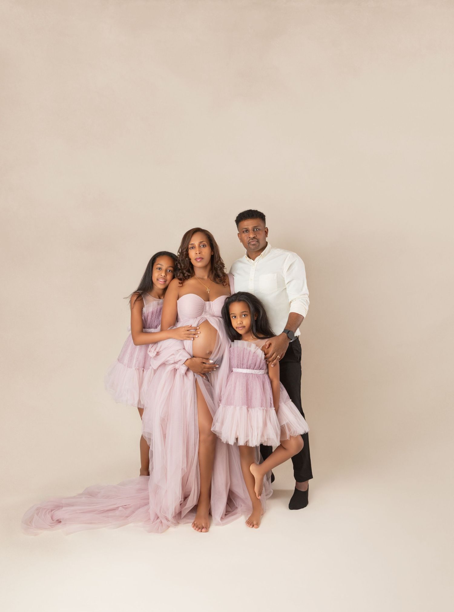 Family of four in lavender outfits poses together for elegant studio maternity portrait.