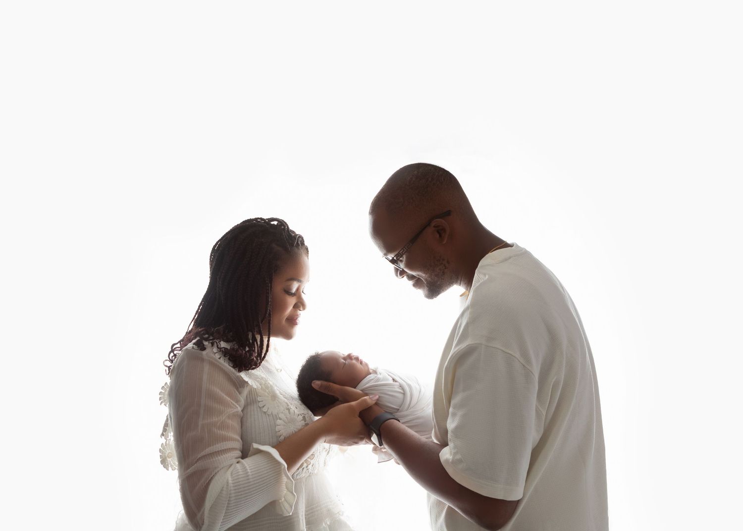 Black family with mother and father lovingly gazing at their newborn baby against a white background.