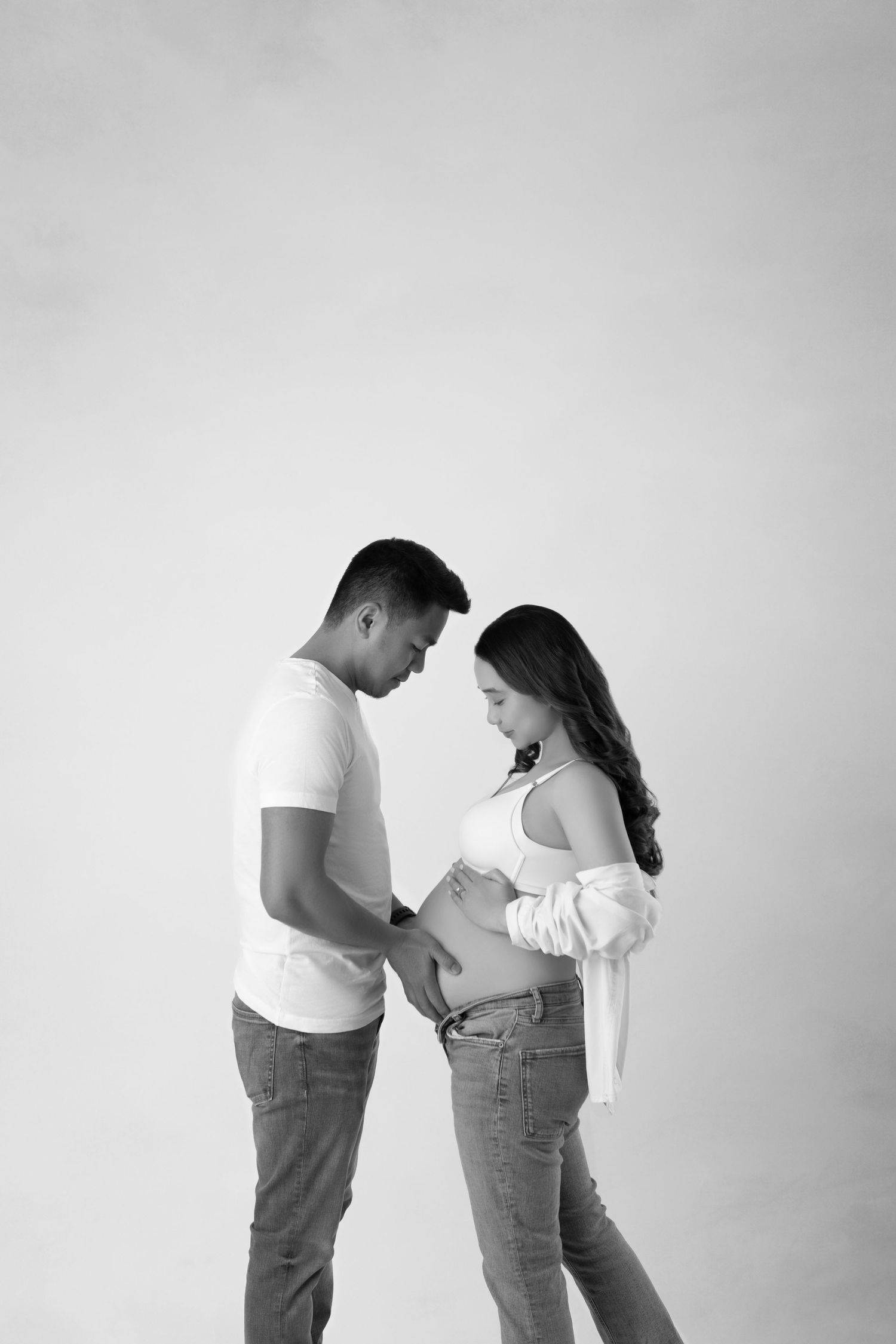 Black and white maternity portrait of couple facing each other, man gently touching pregnant belly.
