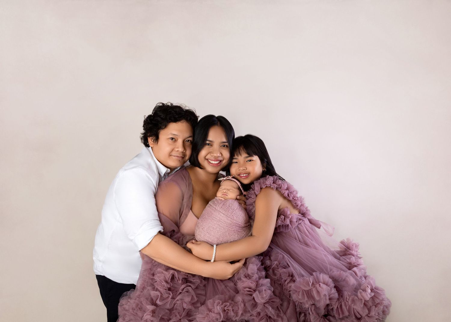 Joyful family portrait with pregnant mom in lavender ruffle gown embracing son and daughter in studio.