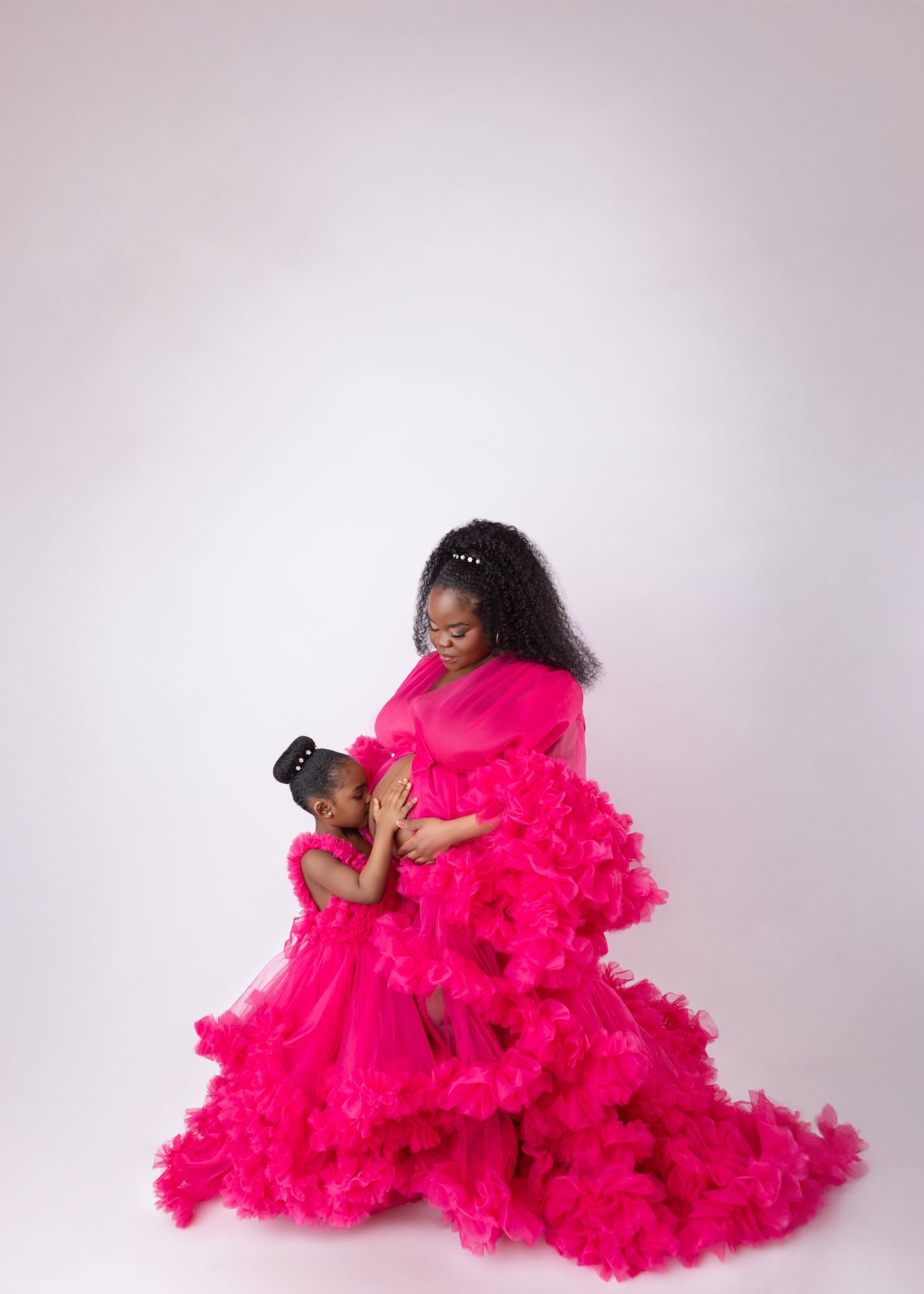 Pregnant woman and young daughter share a sweet moment in matching hot pink ruffle tulle gowns.