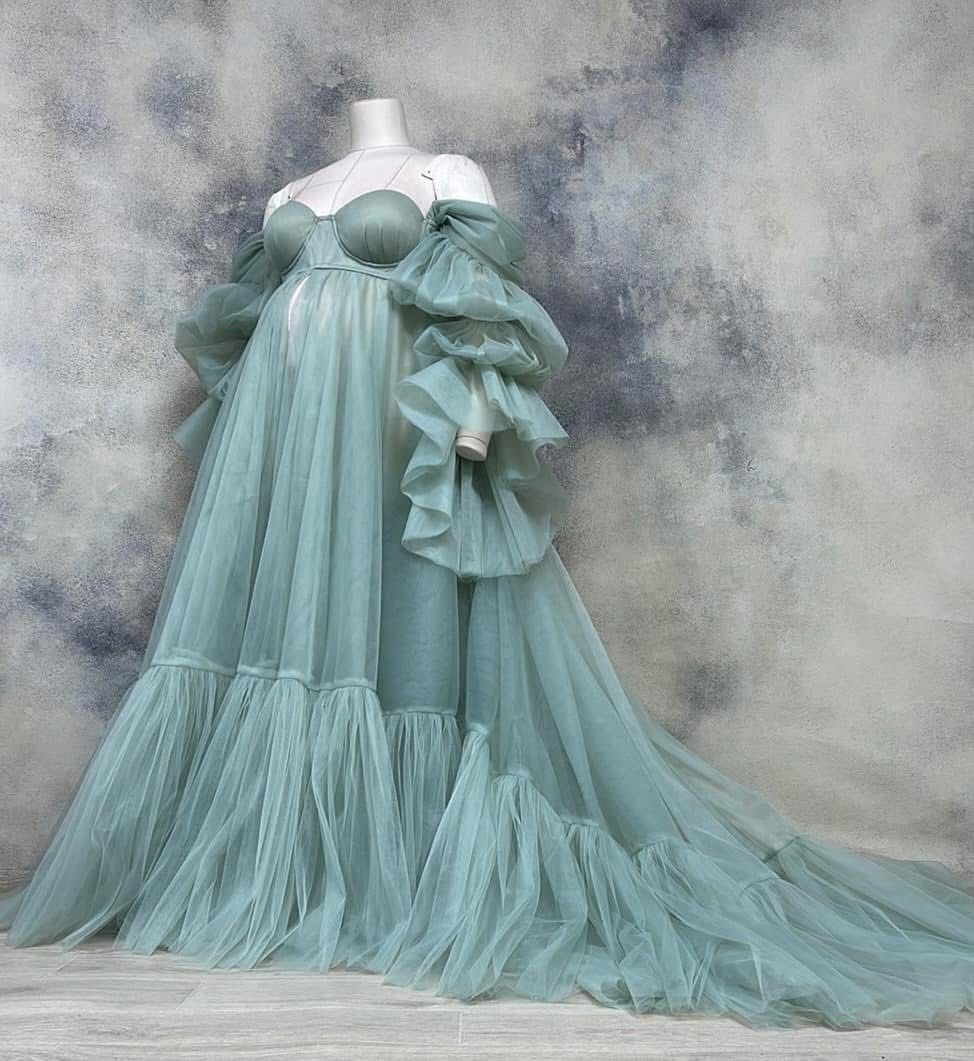 Sage green off-shoulder tulle maternity gown with puff sleeves and flowing tiered skirt on mannequin.