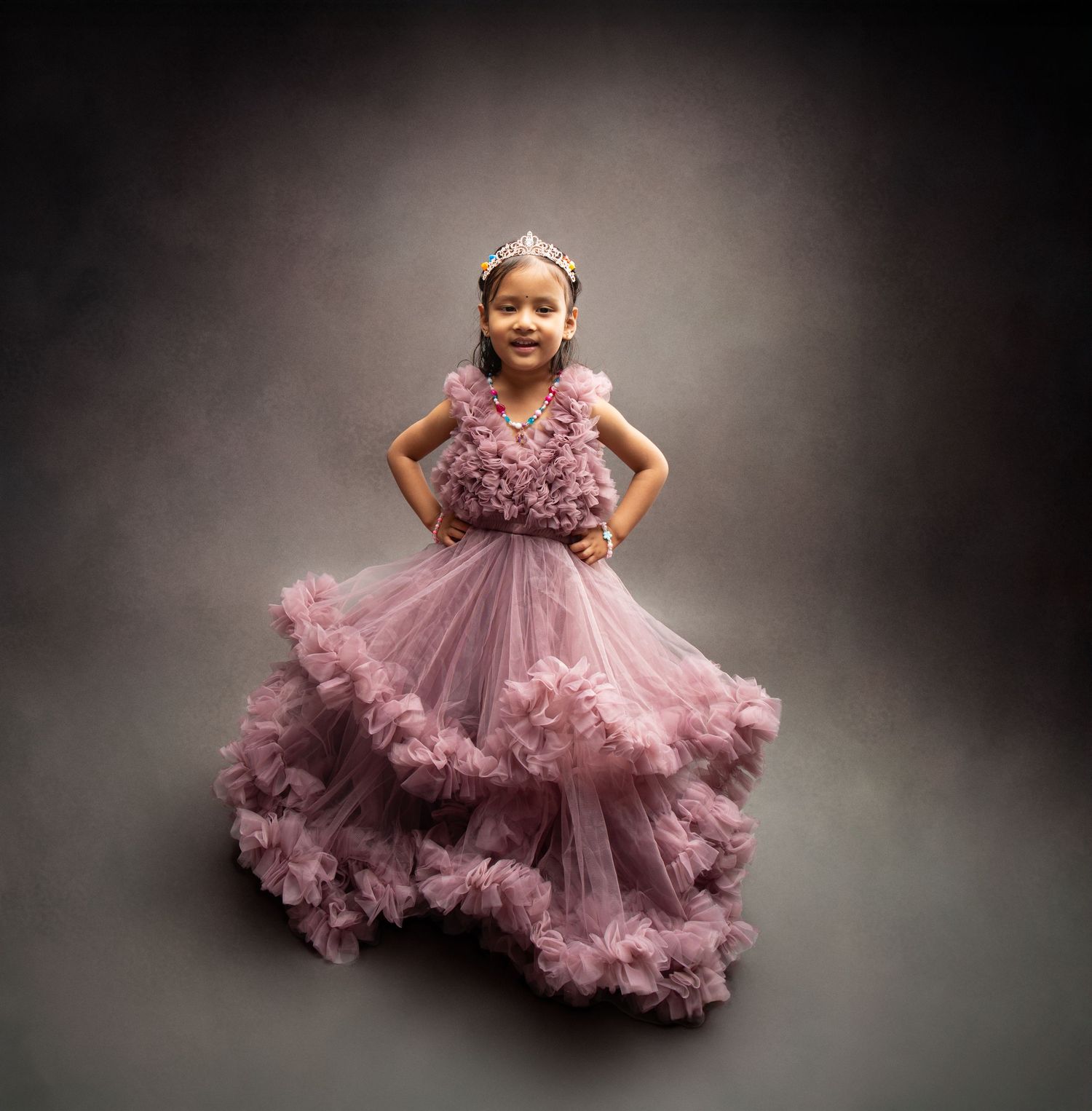 Young girl wearing a pink ruffled tulle princess gown and tiara in a professional photo studio.