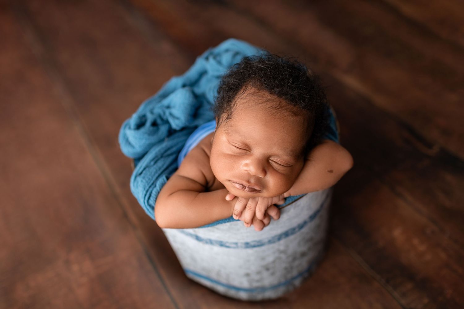 Newborn baby sleeping peacefully in a small bucket wrapped in blue fabric.