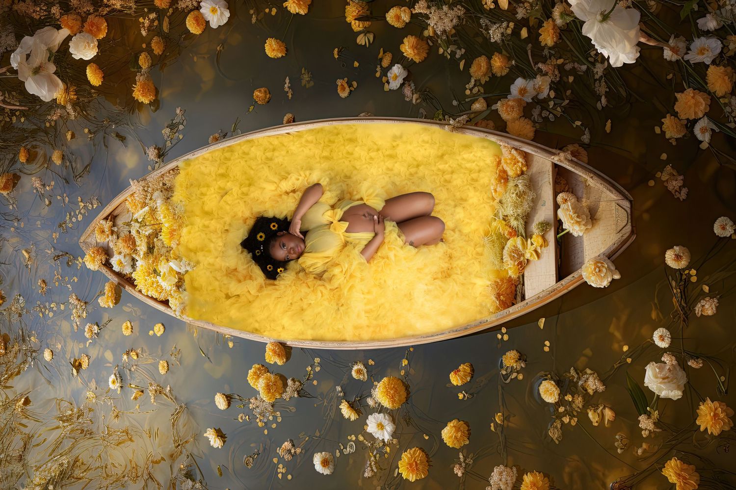 A baby rests in a yellow flower-filled wooden boat floating on water surrounded by white and yellow blooms.