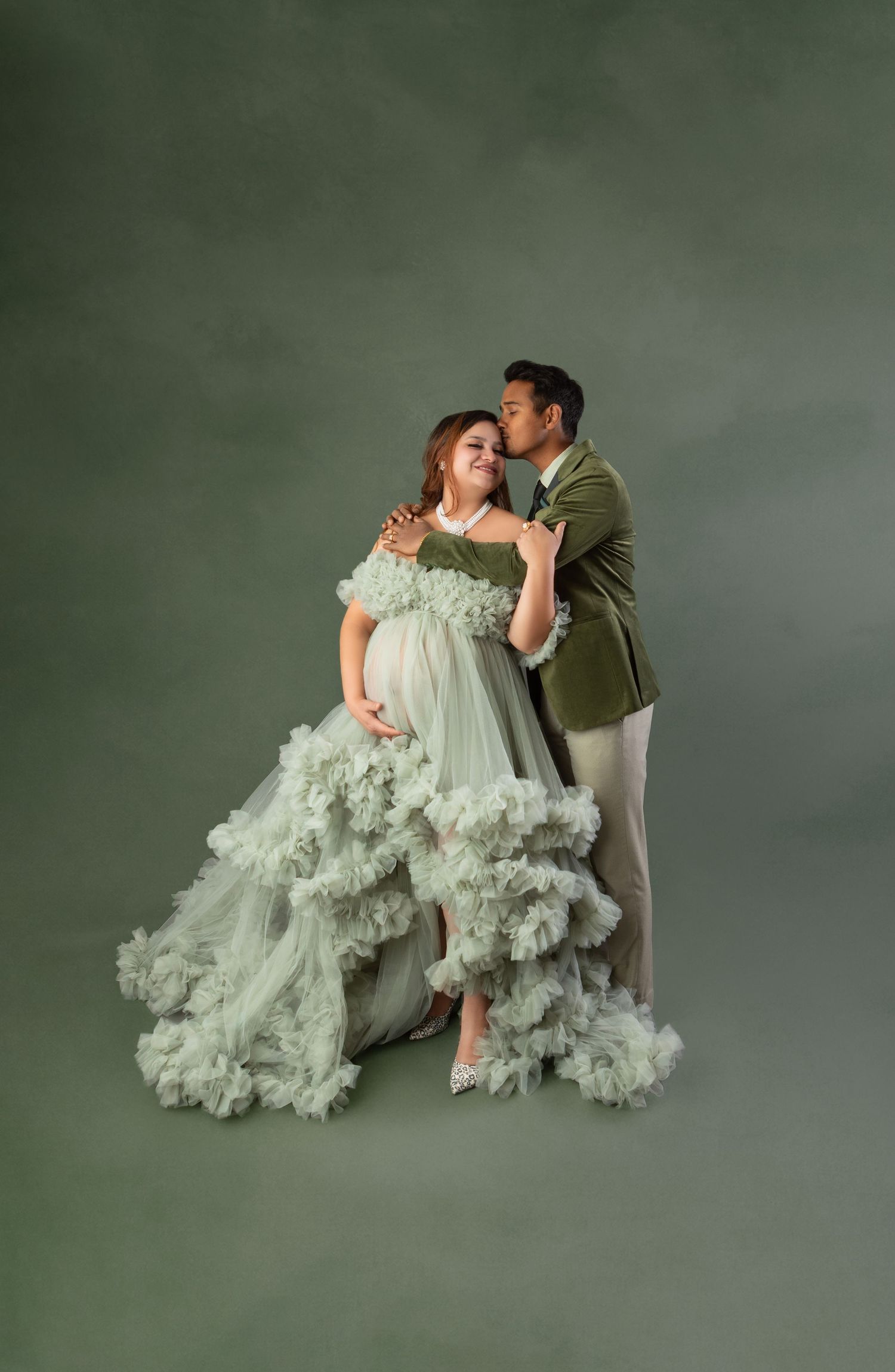 Pregnant woman in sage green ruffled tulle gown with partner in green blazer during maternity photoshoot.