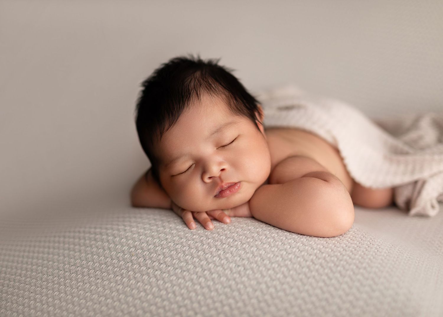 Adorable newborn baby sleeping on a soft white textured blanket with hands under chin.