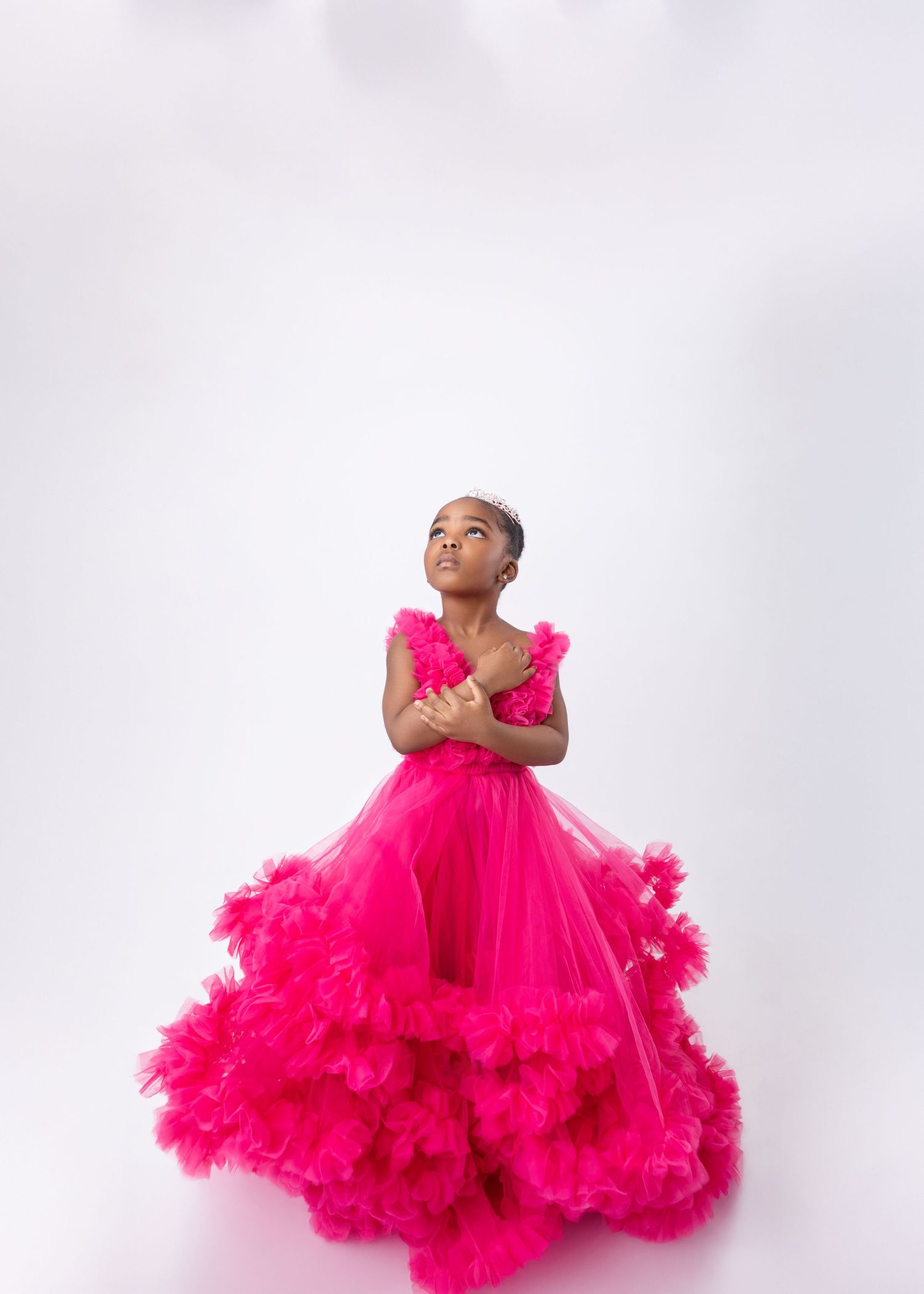 Young girl poses elegantly in a voluminous hot pink ruffle tulle ball gown on white background.