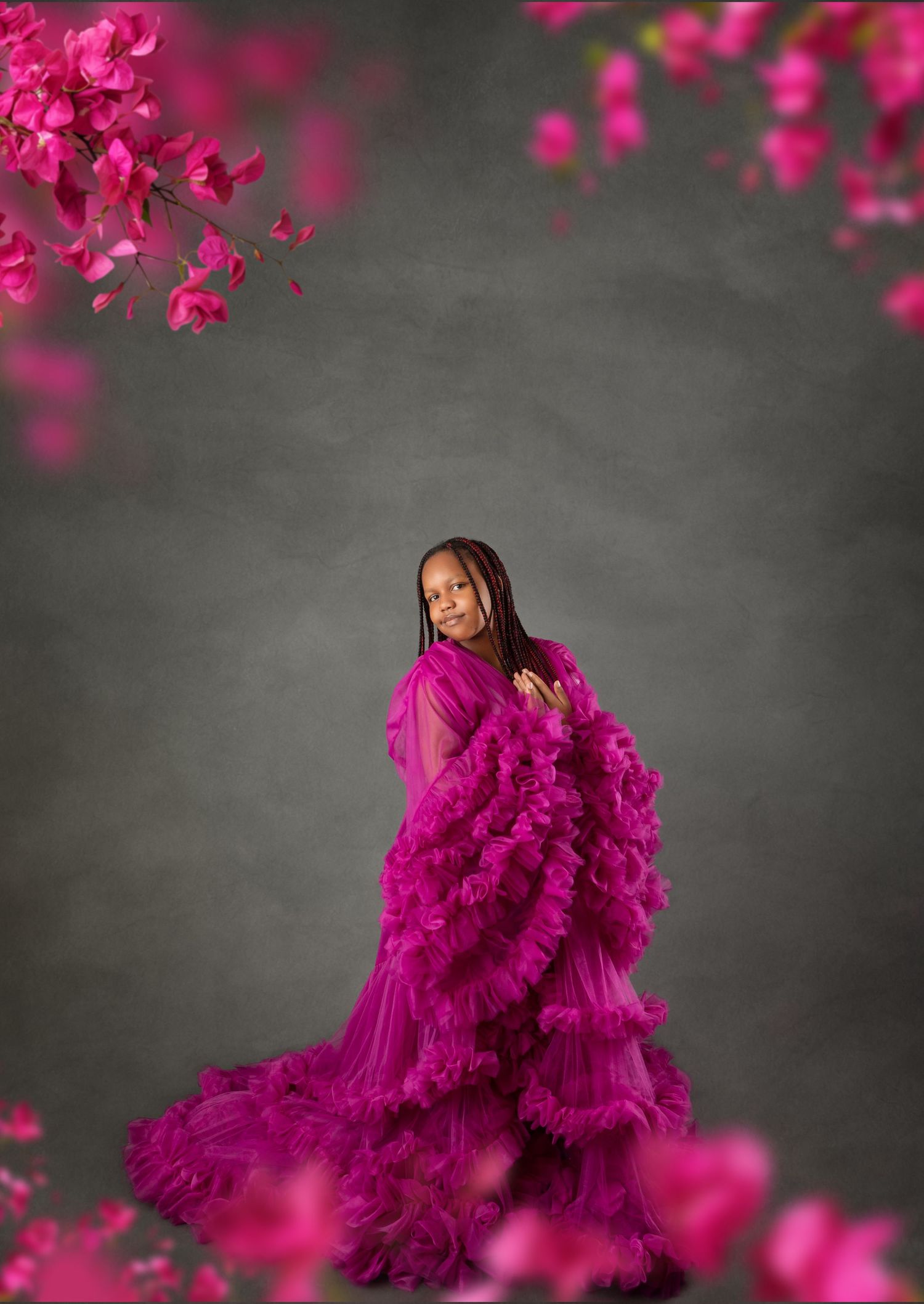 Young girl in a stunning magenta ruffle tulle gown poses gracefully among vibrant pink bougainvillea flowers.