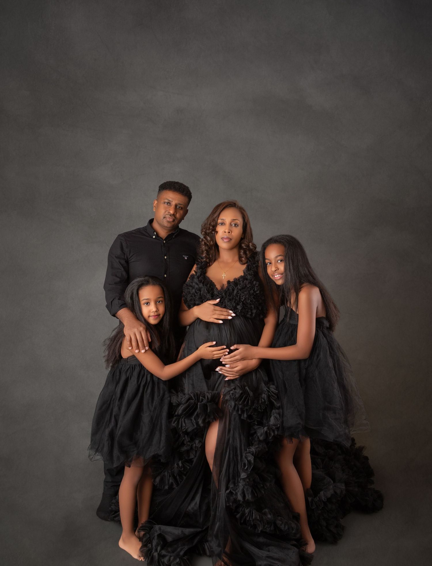 Family maternity photo in matching black outfits with pregnant mother in lace gown and two daughters.