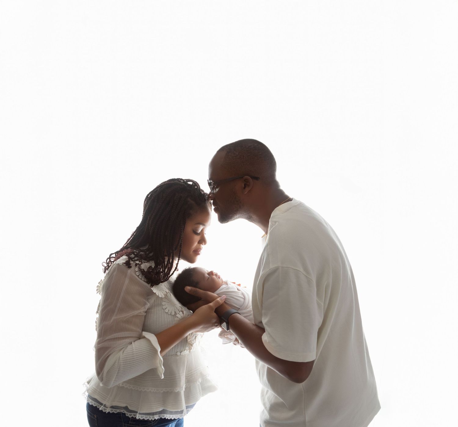 Loving Black parents sharing a tender moment while holding their newborn baby together.