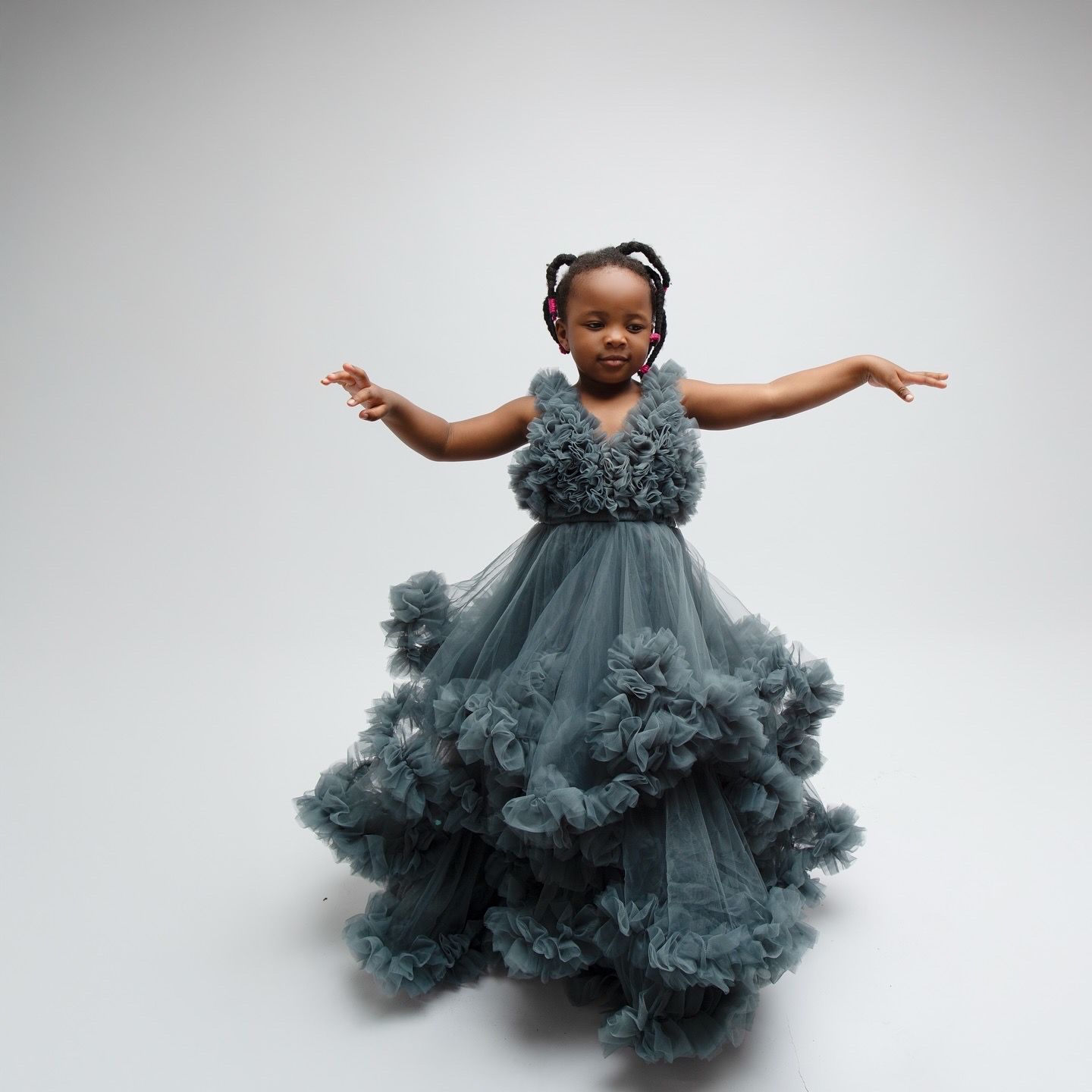 Young girl in a dusty blue ruffled tulle ball gown spreading her arms wide in a studio.