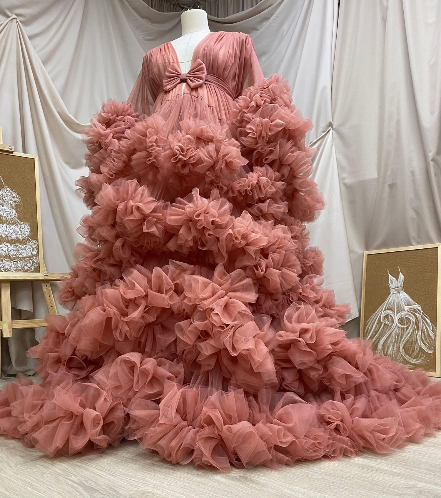 Luxurious dusty rose ruffled tulle maternity gown with long sleeves and voluminous layered skirt on mannequin.