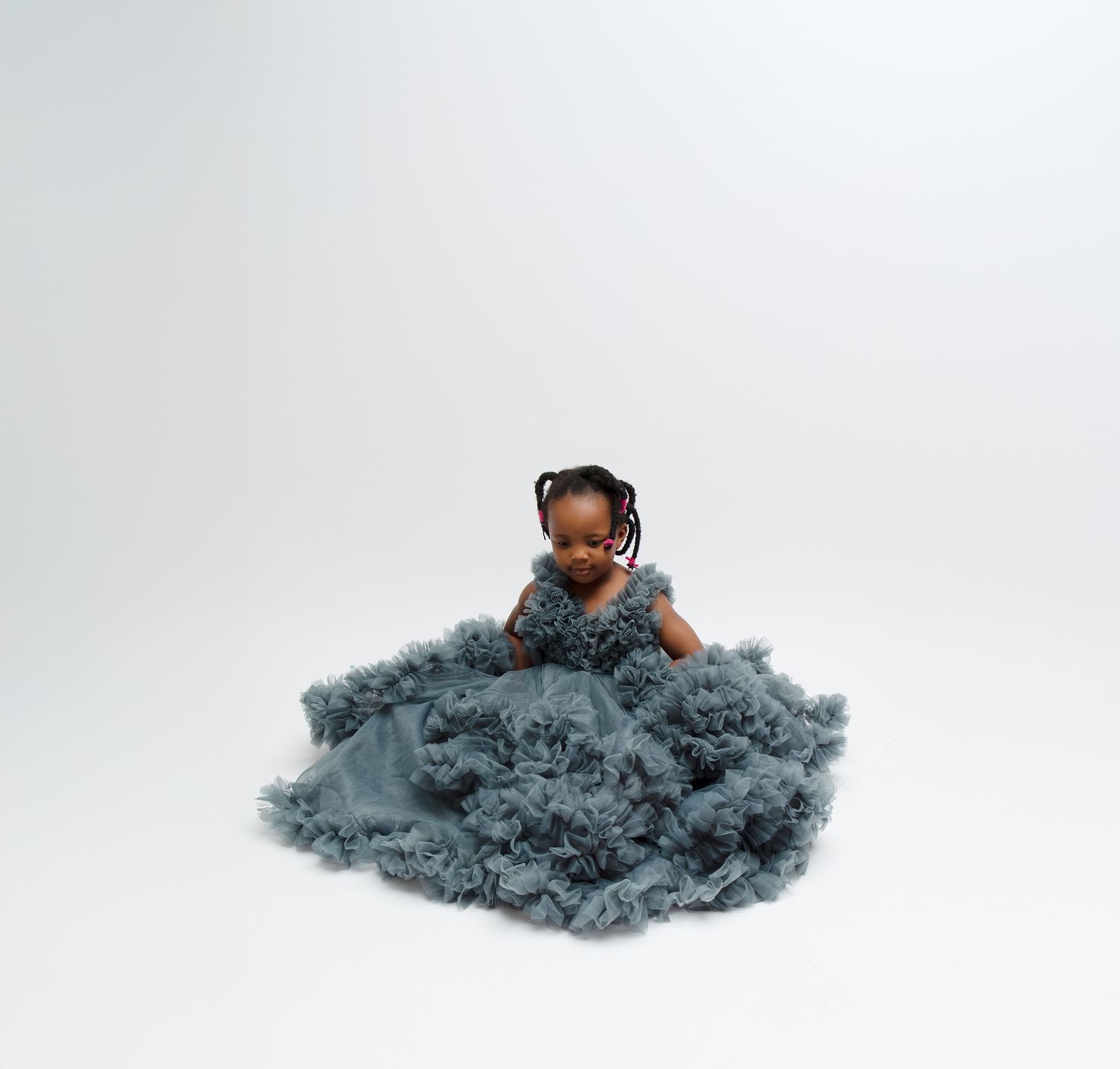 Young girl in a voluminous dusty blue ruffle tulle gown sitting on a white studio floor.