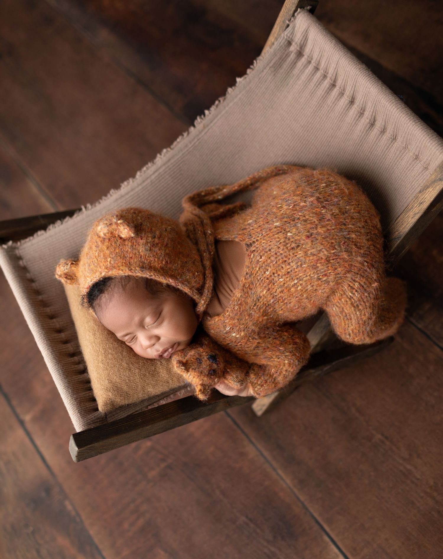 Newborn baby in brown knit bear outfit sleeping in a wooden crib.