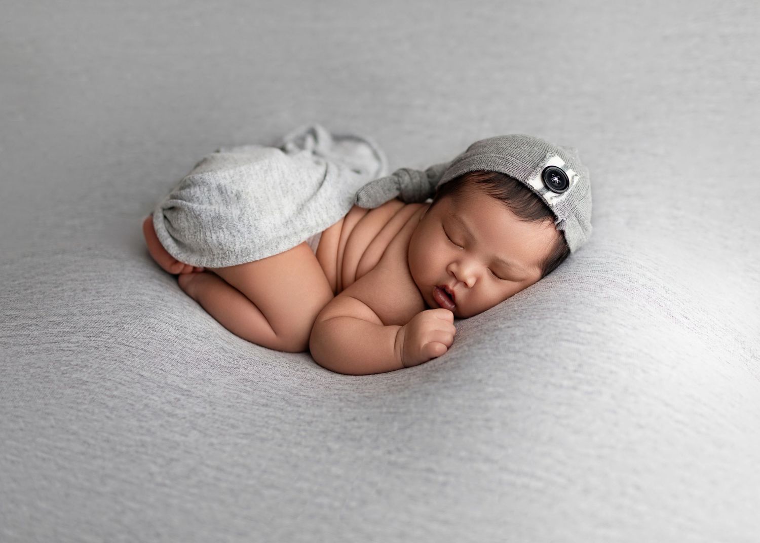 Curled newborn baby sleeping in a gray elephant outfit on a soft gray background.